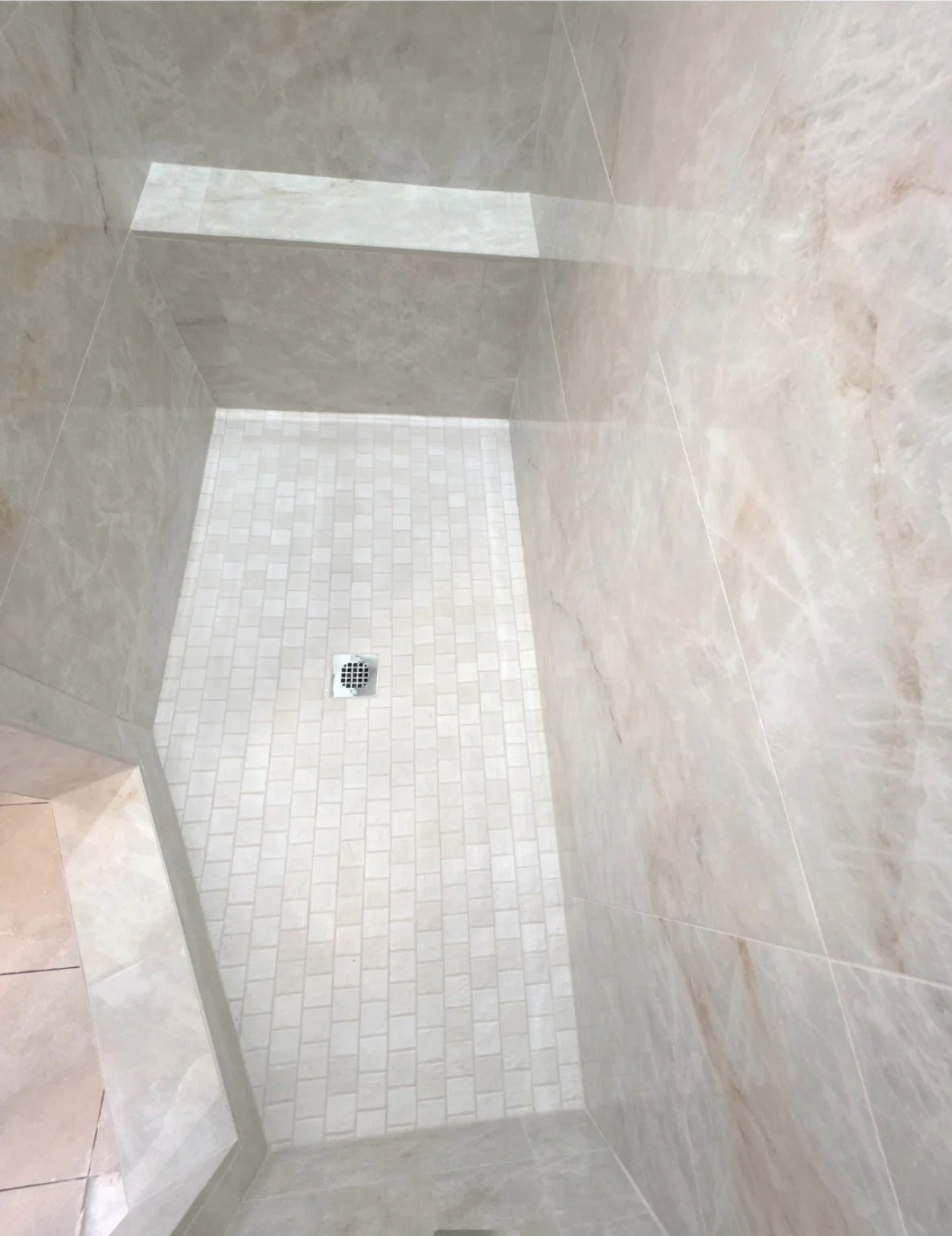 Finished beige tile shower with a bench, rectangular mosaic floor, and square drain