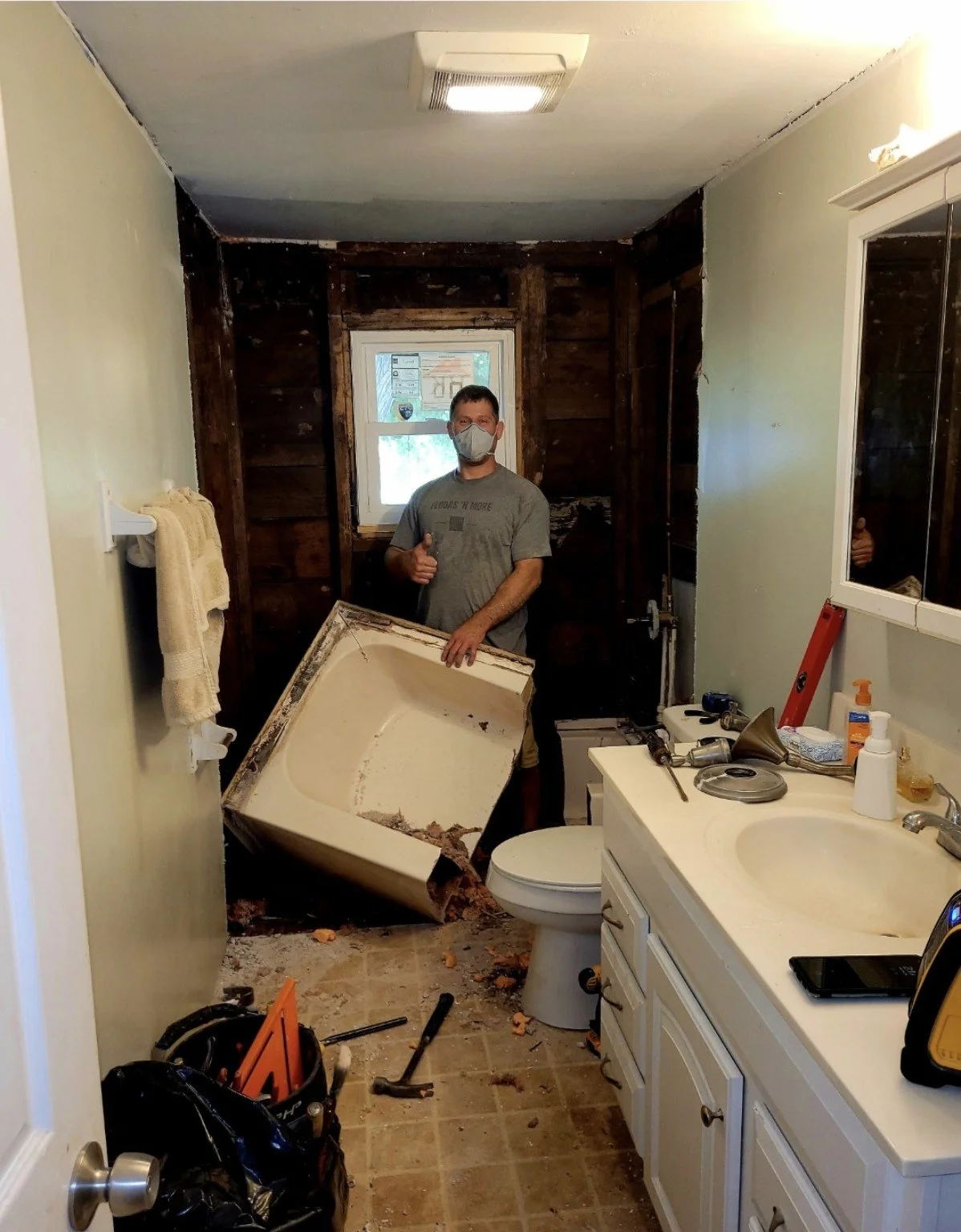 Jesse removing an old tub surround in a bathroom with opened walls around a window