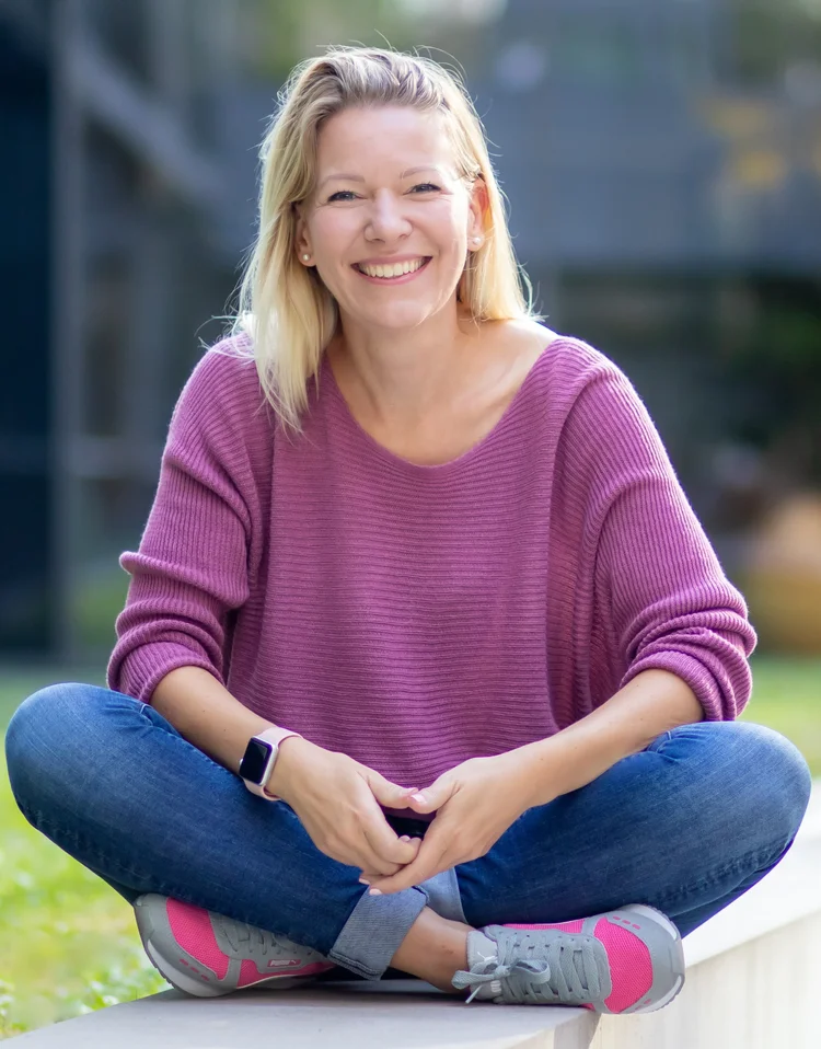 Denise Spekowius, Sales Coach und Autorin, lächelnd im Schneidersitz auf einer Mauer im Freien