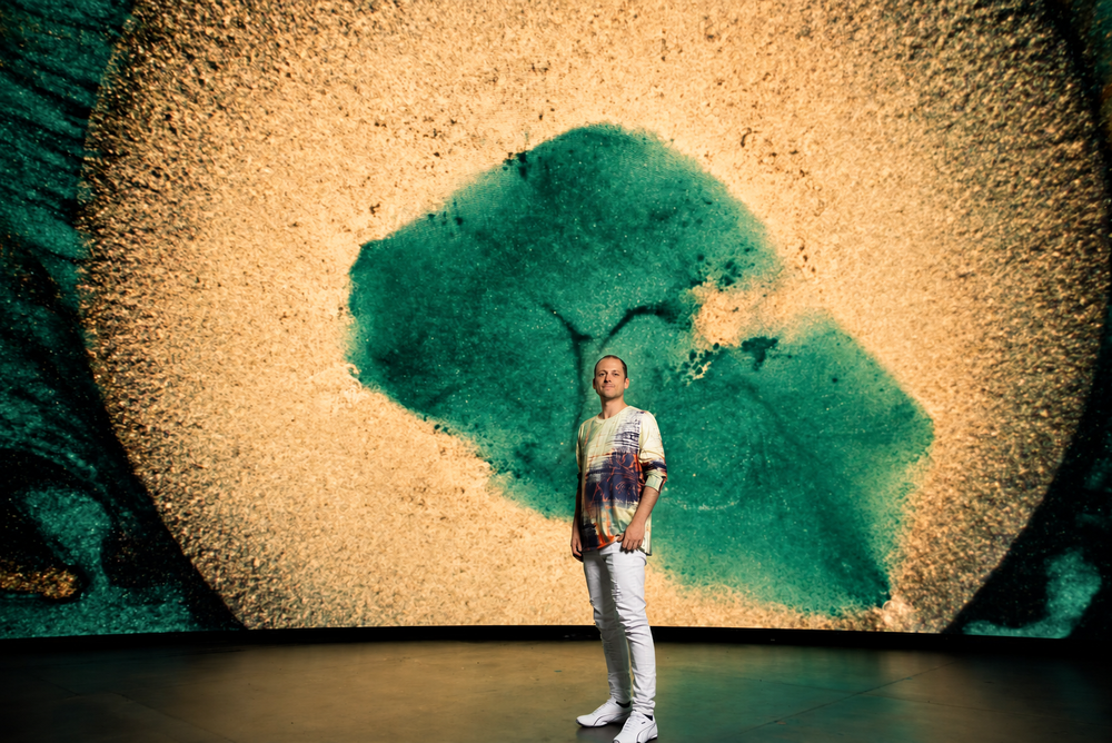 Composer Ricardo Romaneiro stands in front of a large abstract liquid-light projection.