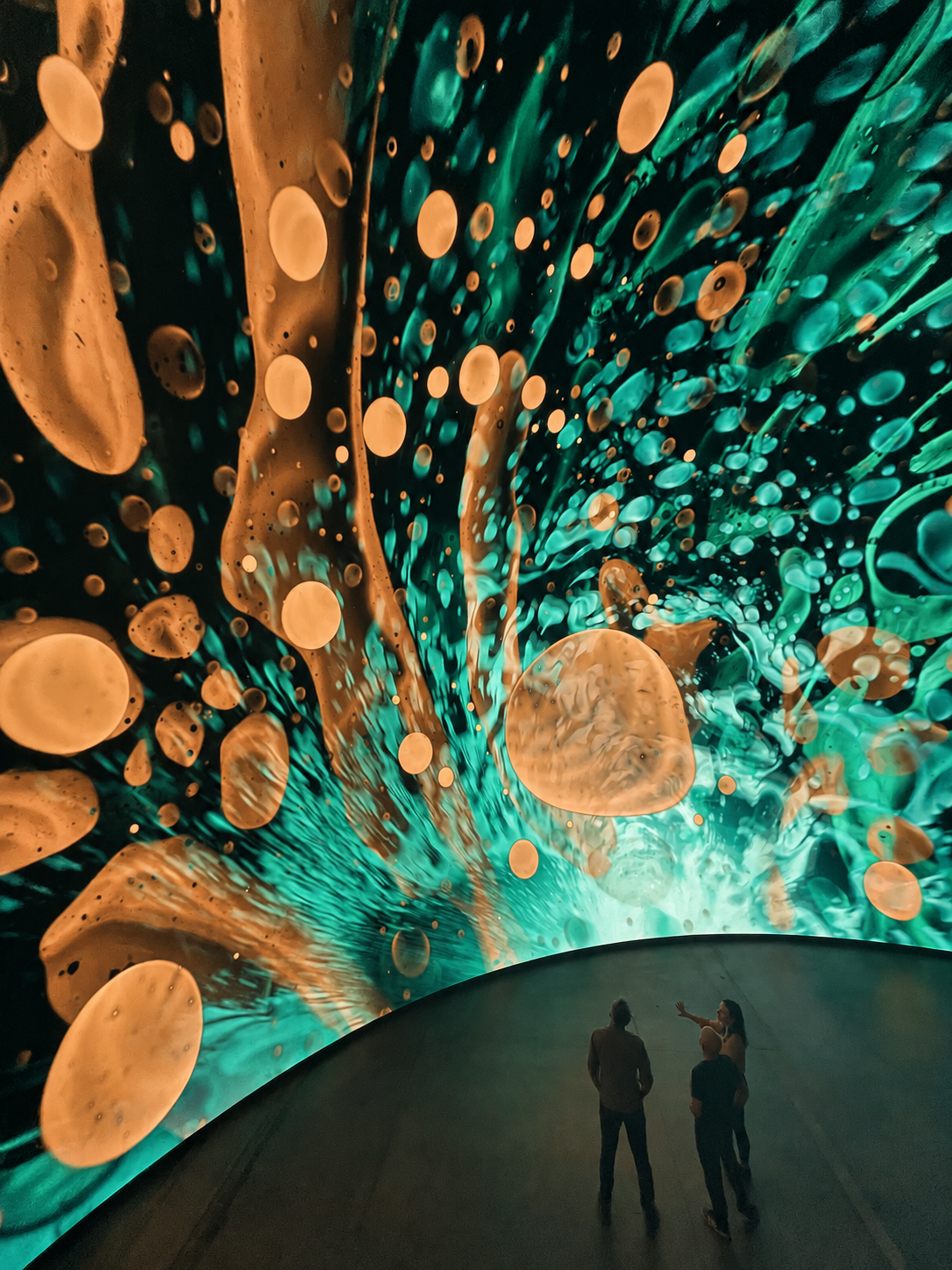 Copper and verdigris forms ripple across an abstract liquid-light projection.