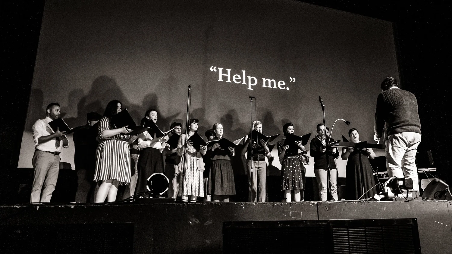 Verdigris Ensemble and conductor perform Betty’s Notebook beneath the projected words ‘Help me.’