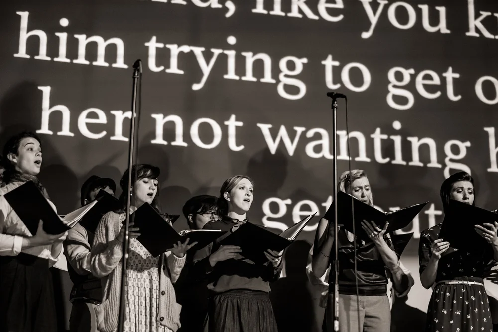 Verdigris singers perform in front of enlarged fragments of the radio transcript.