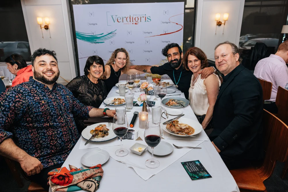 Guests gather around a dinner table with a Verdigris Ensemble backdrop.