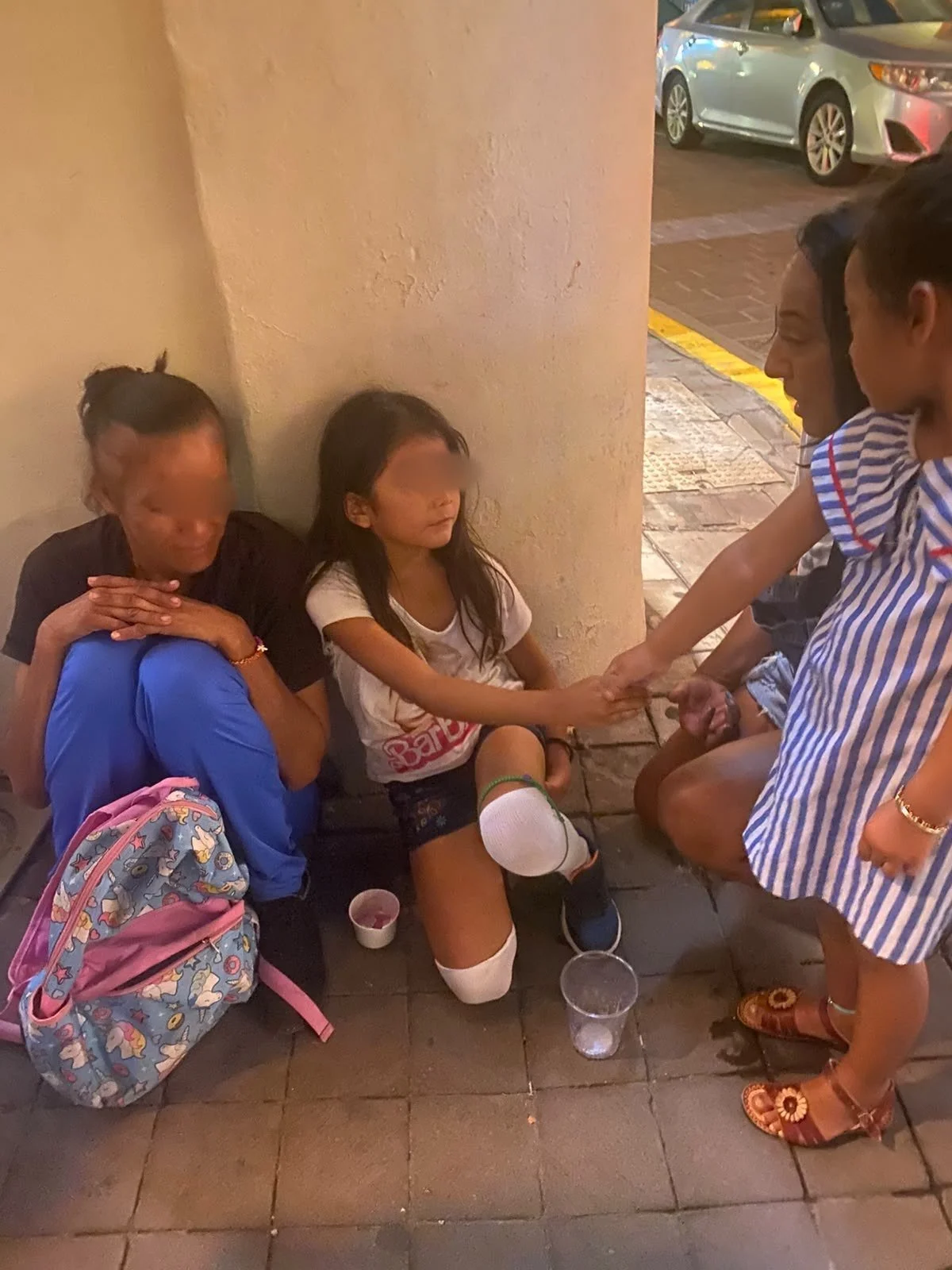 Care on the sidewalk—eyes of seated woman and girl softly obscured