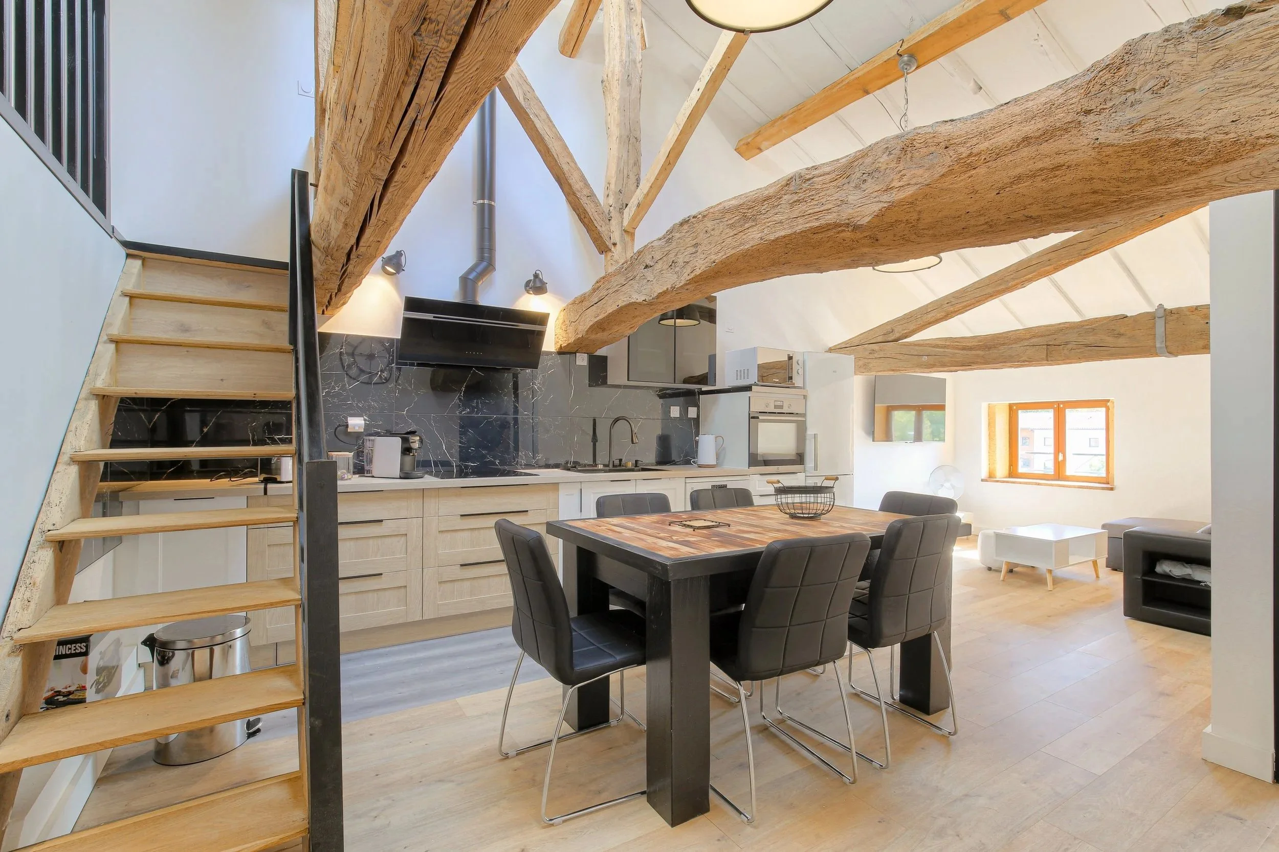 Cuisine ouverte rénovée sous charpente apparente, table et escalier bois – DõmHõ