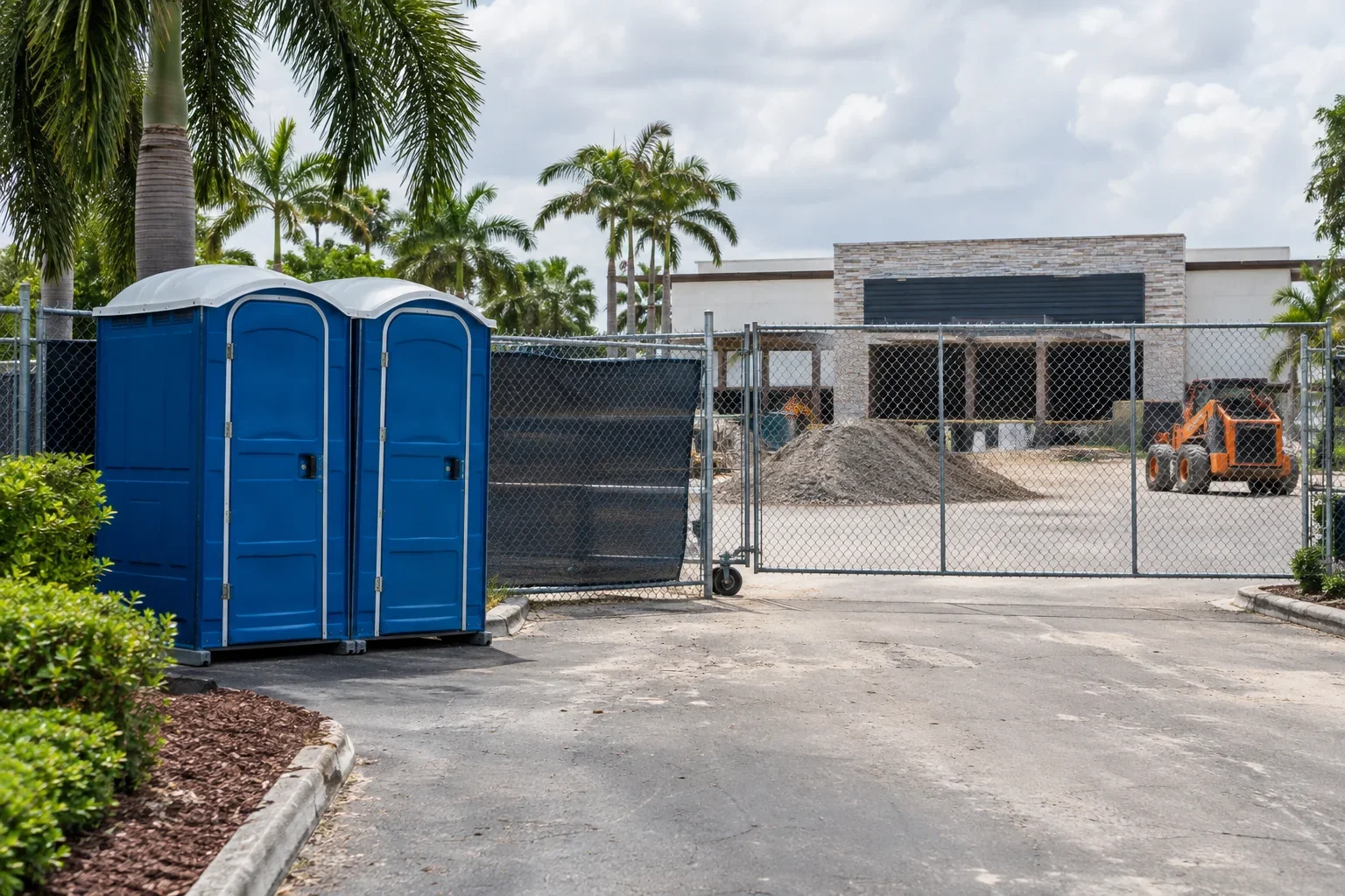 Portable toilets positioned beside a gated temporary construction perimeter for Construction Toilets & Fencing near me in Davie, FL.