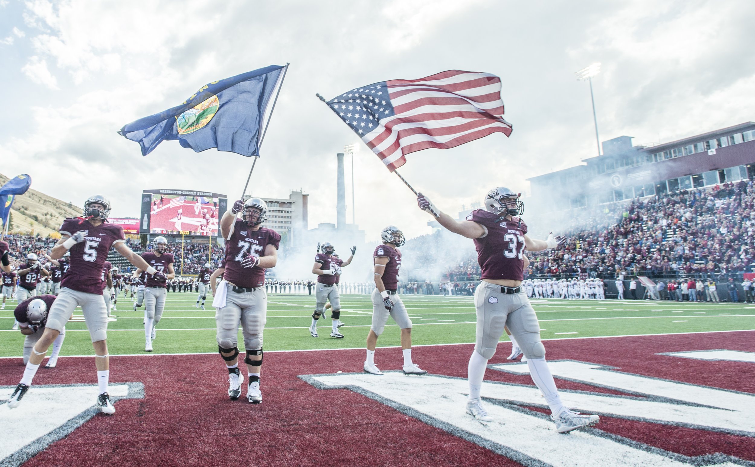 Griz football players carrying flags onto the field