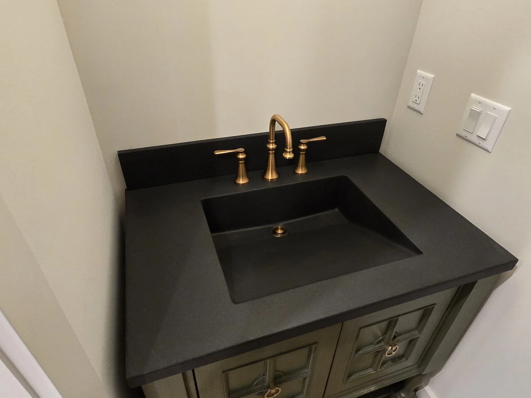 Black ramp sink with a visible standard drain and brass faucet