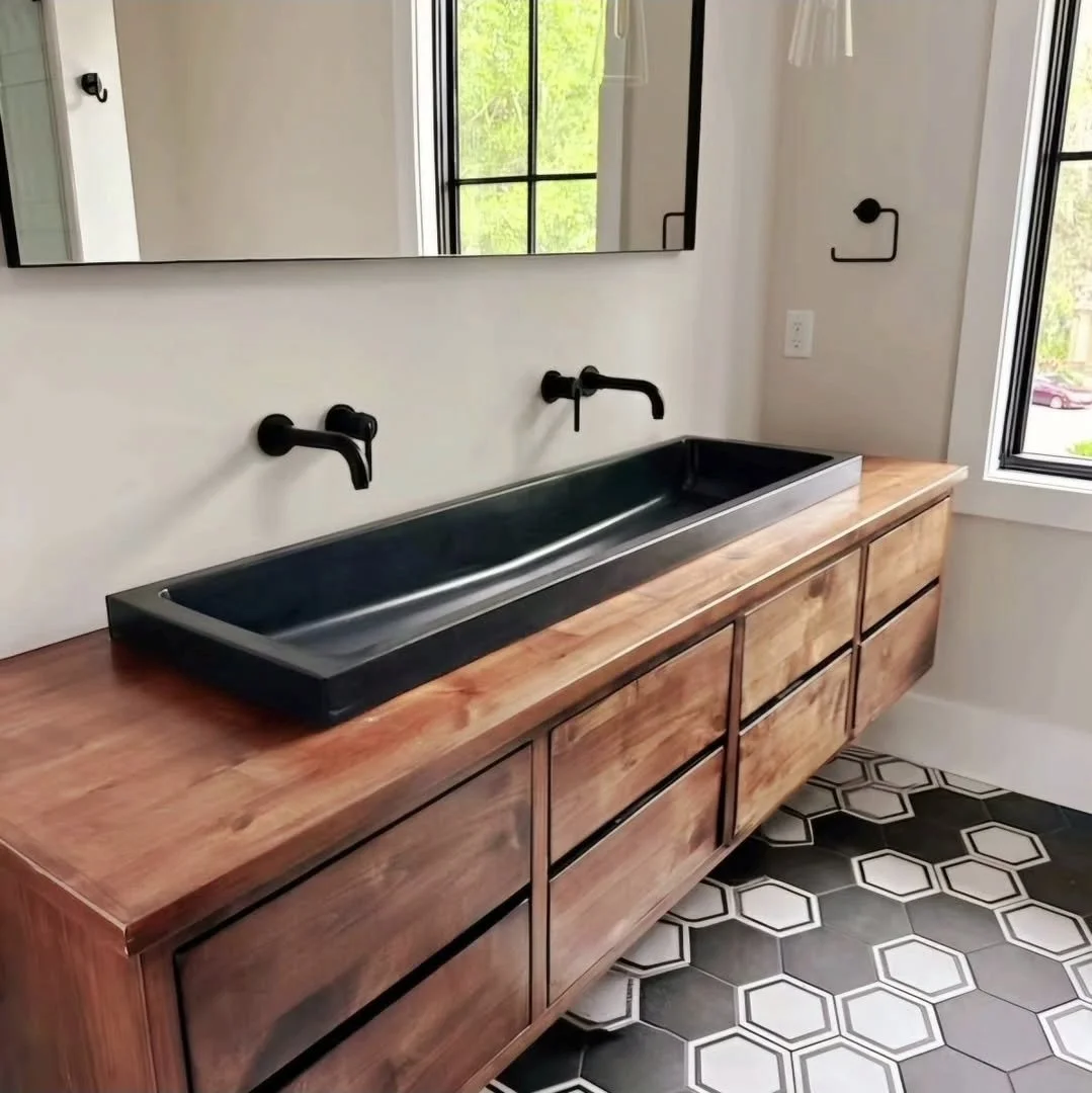 Black trough sink installed on a wood vanity with two wall-mounted faucets