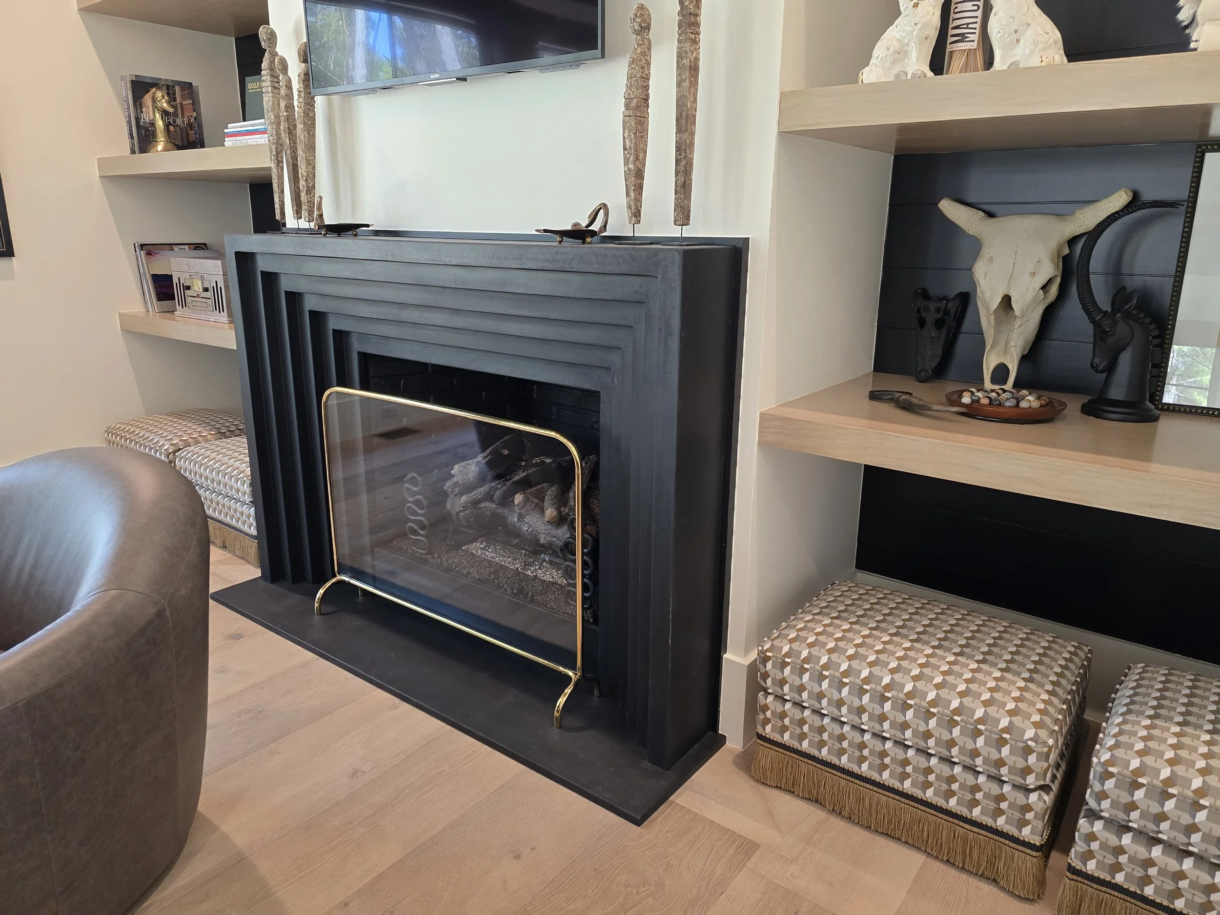A wider view of the black stepped Blackline fireplace with leather chair and wood shelving on both sides