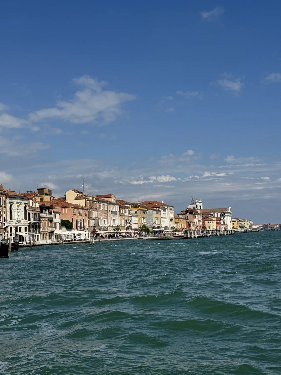 Colorful historic buildings lining the Venetian lagoon beneath a blue sky.