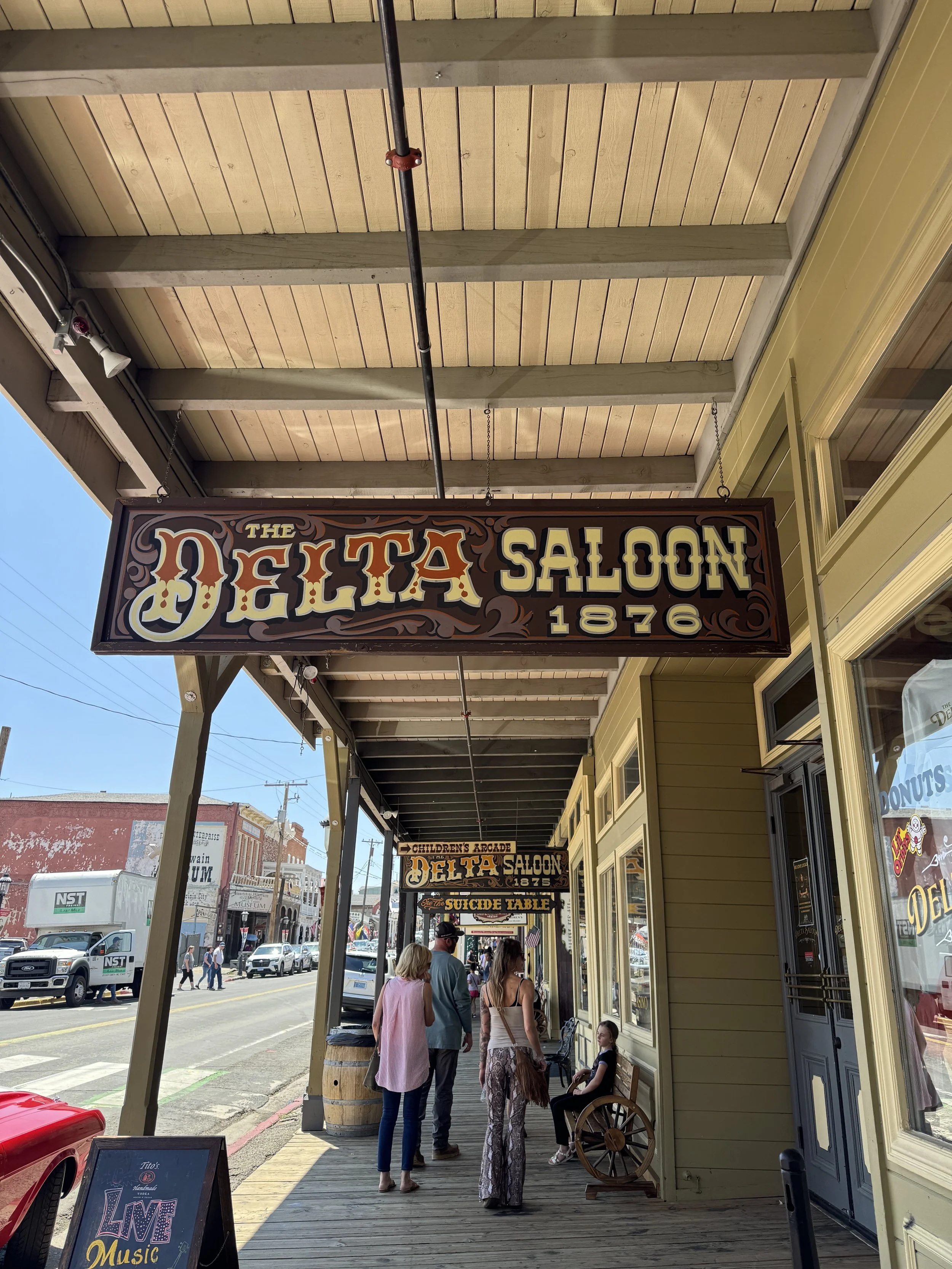 Historic Delta Saloon signs hanging above the wooden sidewalk in Virginia City, including a sign for the Suicide Table.