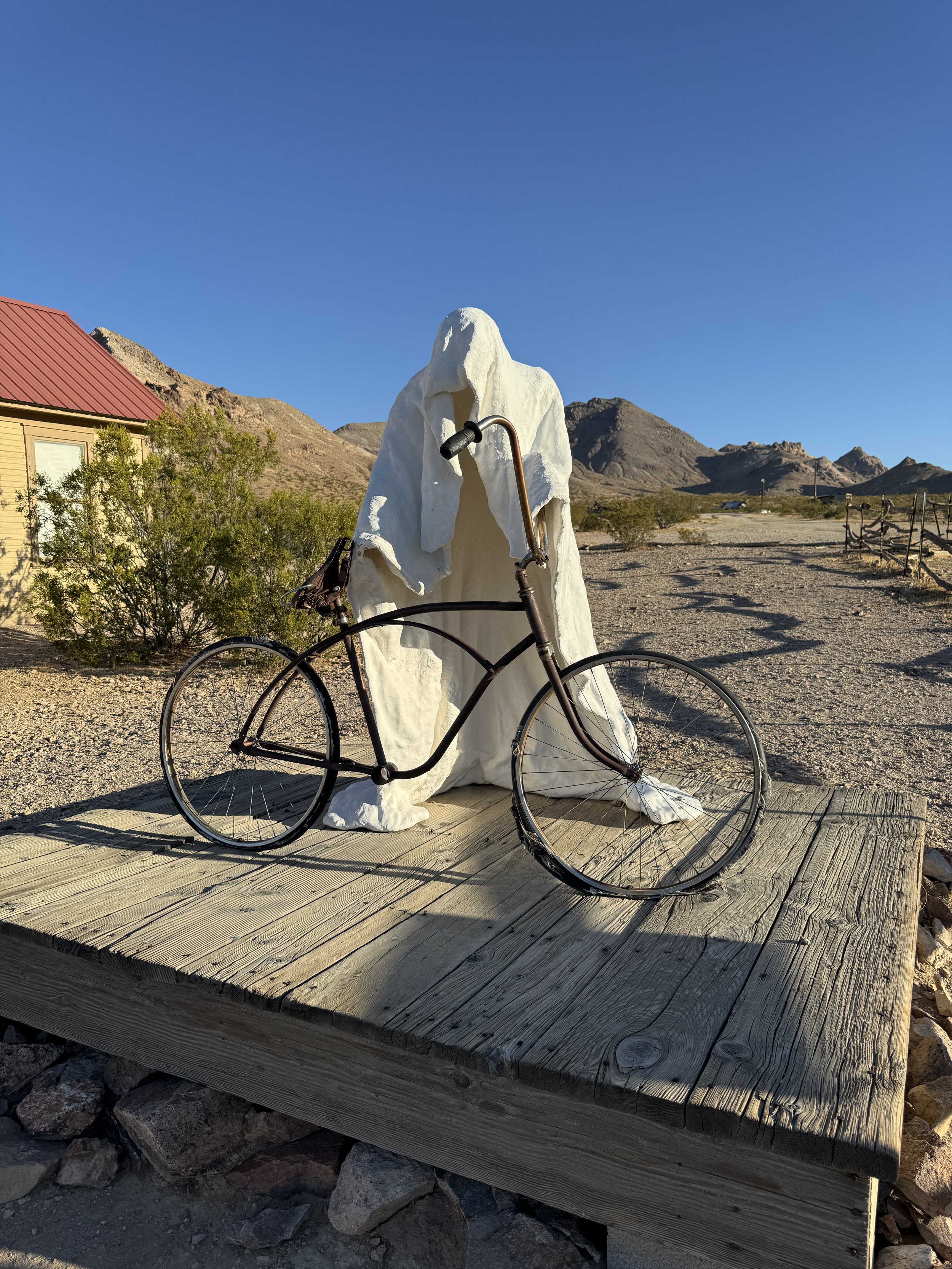 White shrouded ghost sculpture standing behind a vintage bicycle at the Goldwell Open Air Museum near Rhyolite, Nevada.