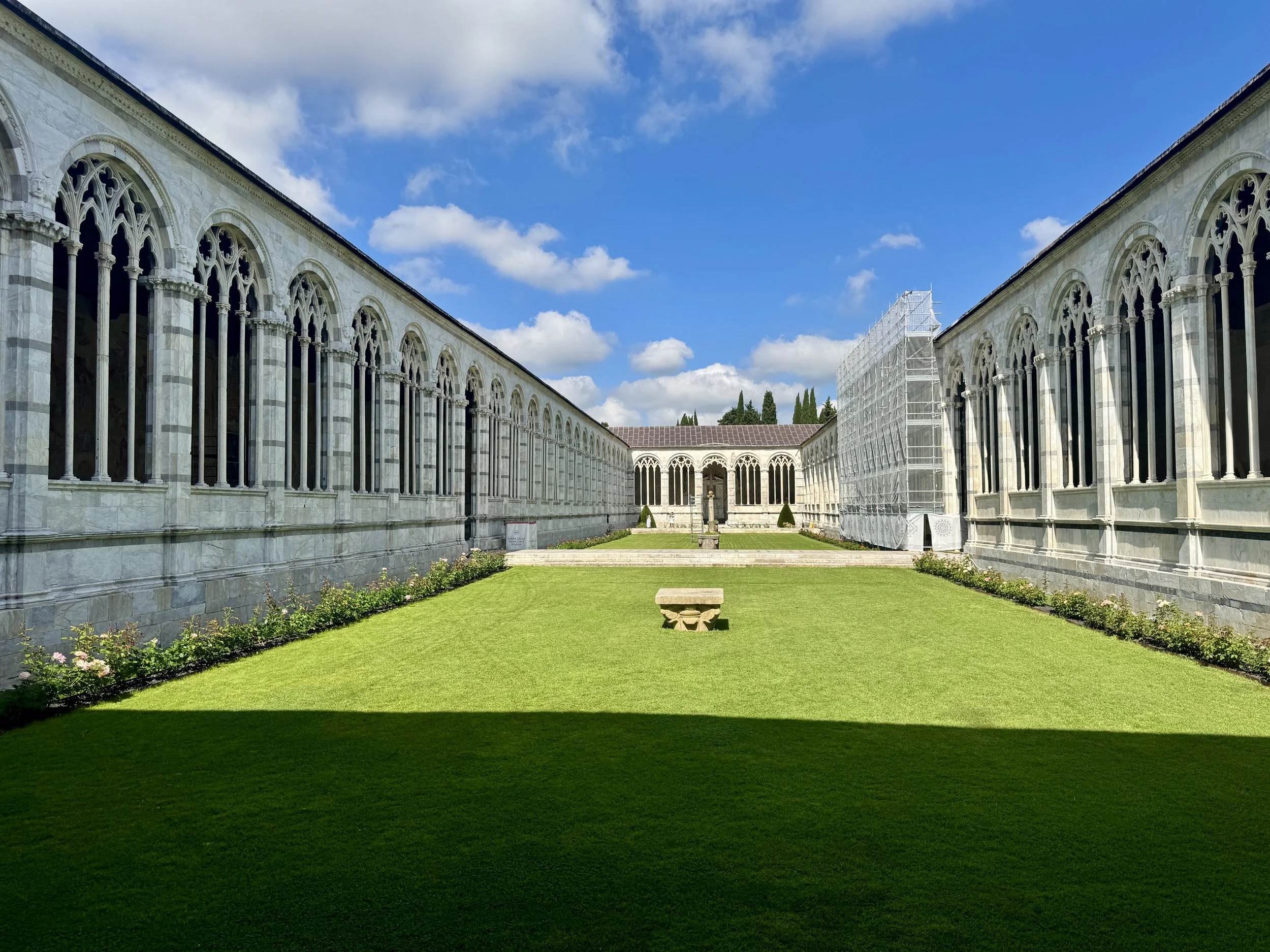 Sunlit Gothic cloister and green central courtyard of Camposanto Monumentale.