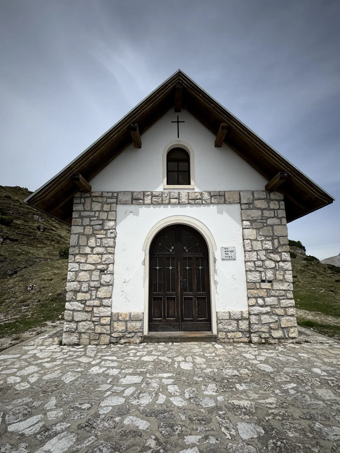 Small stone memorial chapel on Monte Piana with a cross above its arched doorway.