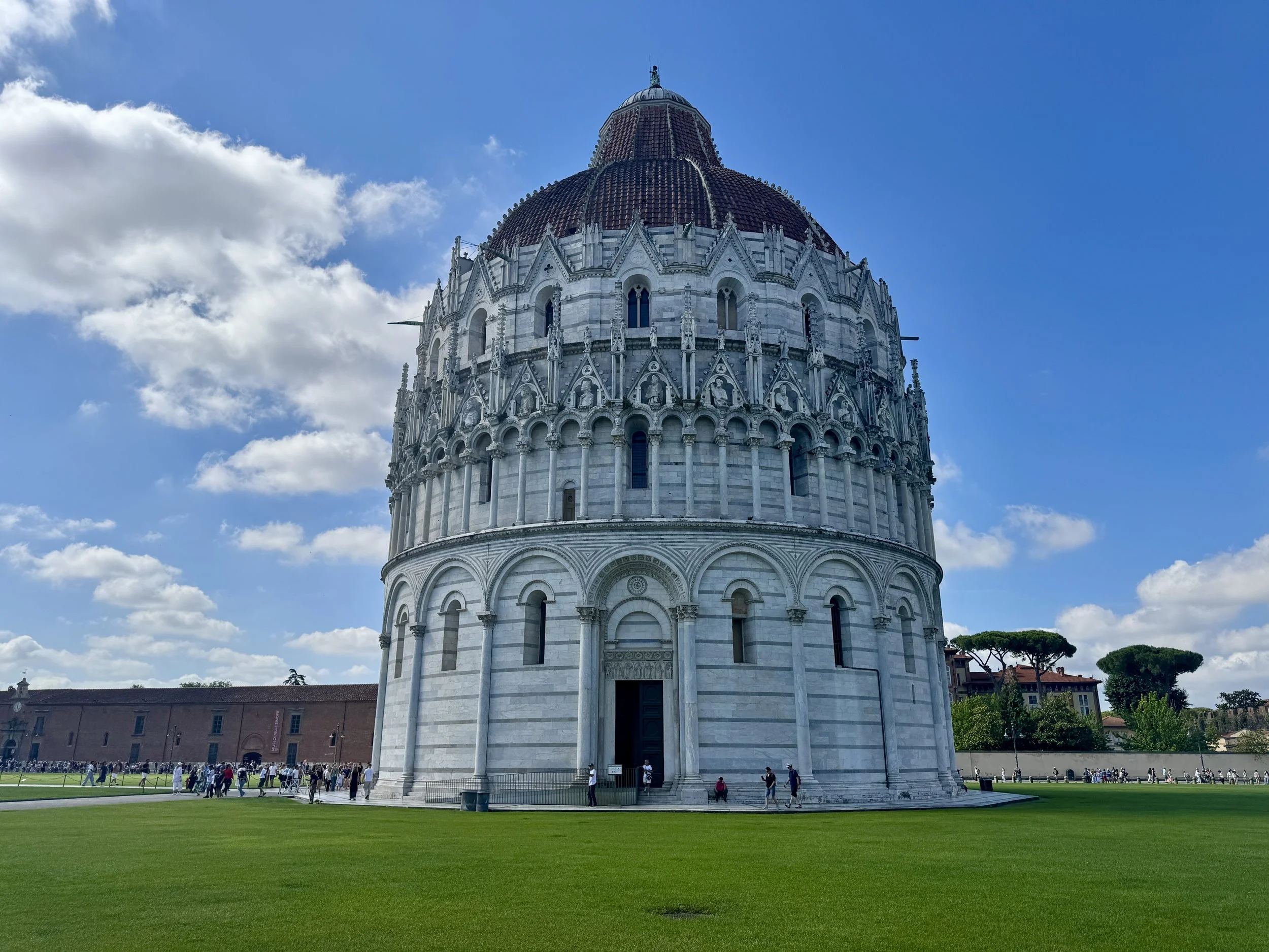 Pisa Baptistery beneath a bright blue sky in Piazza dei Miracoli.