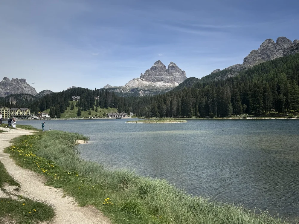 Calm water of Lago di Misurina with lakeside buildings, forested slopes and Tre Cime beyond.