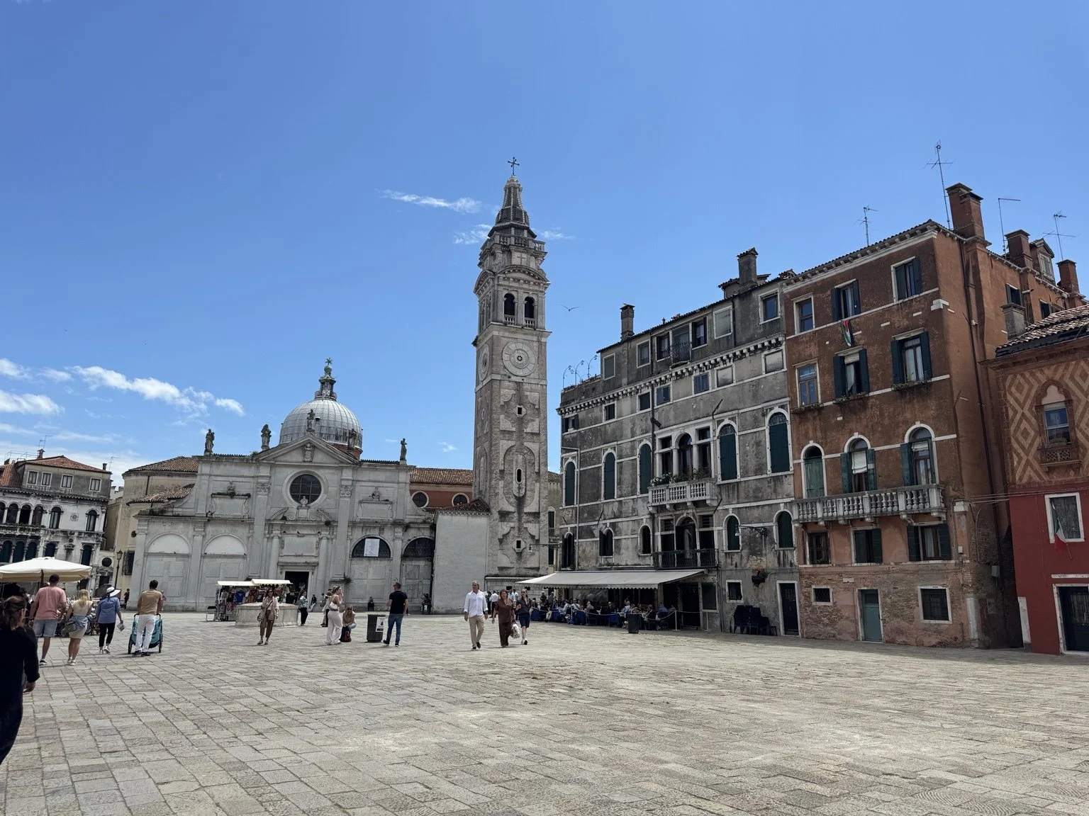 Venetian square with a domed church, bell tower and historic buildings beneath a blue sky.