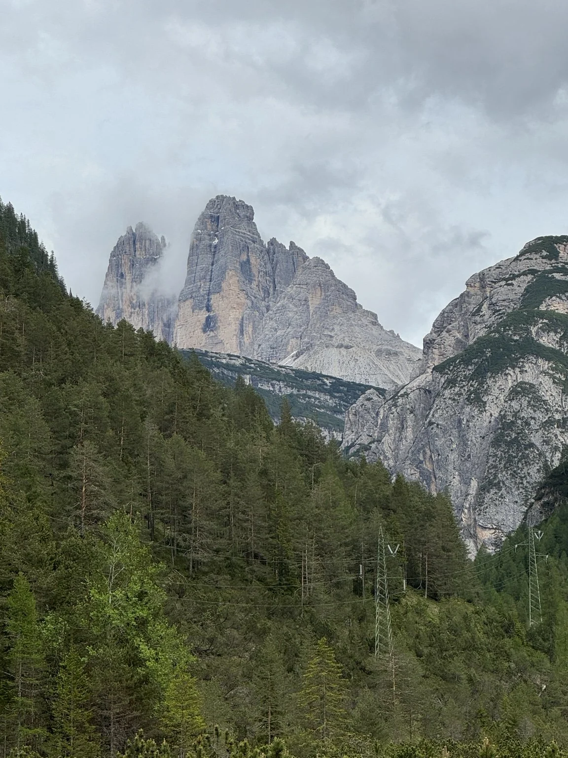 Tre Cime di Lavaredo rising through low clouds above the green Alpine valley.
