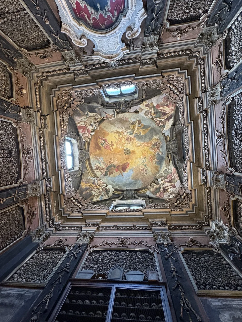 Baroque ceiling fresco surrounded by skulls and bones inside San Bernardino alle Ossa in Milan
