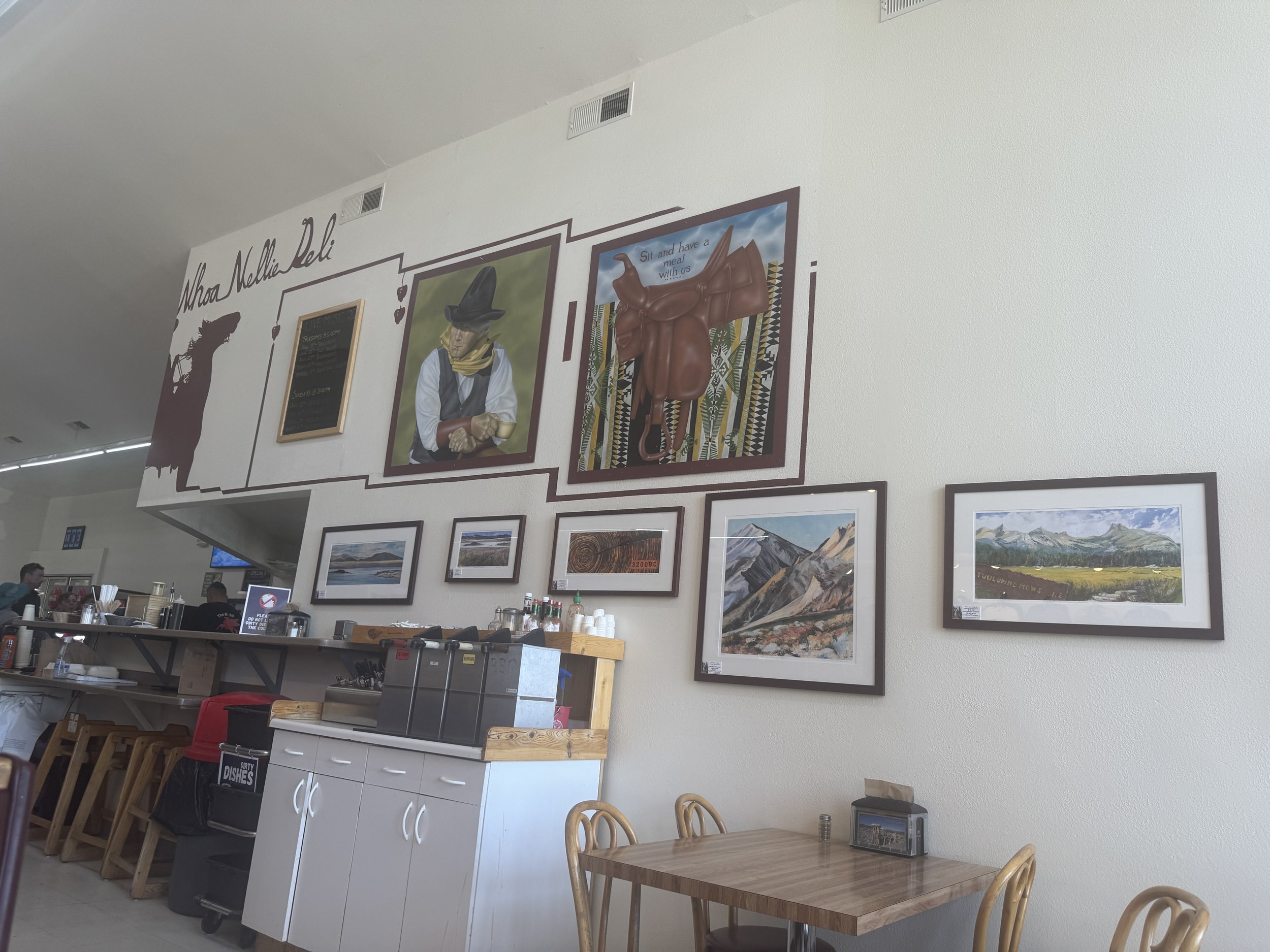 Interior of the Whoa Nellie Deli in Lee Vining with Western artwork and framed Eastern Sierra landscapes above the counter.