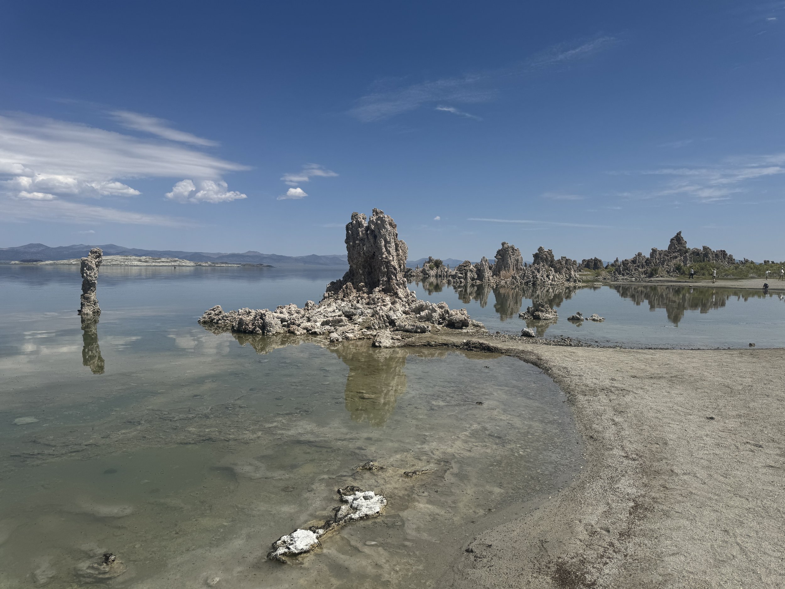 Large limestone tufa towers and their reflections beside the curved shoreline at Mono Lake.