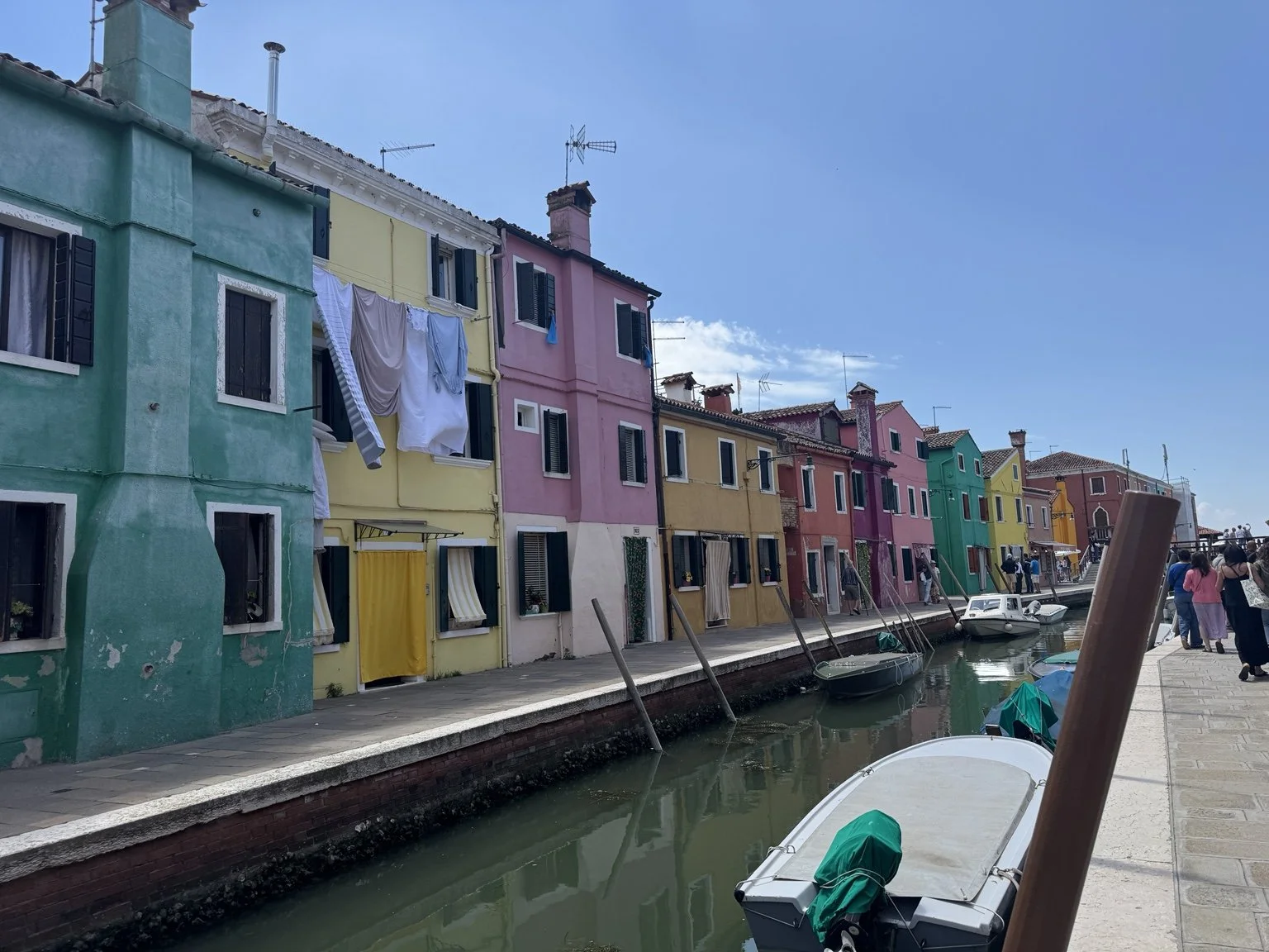 Burano canal lined with turquoise, yellow and pink houses, hanging laundry and boats.