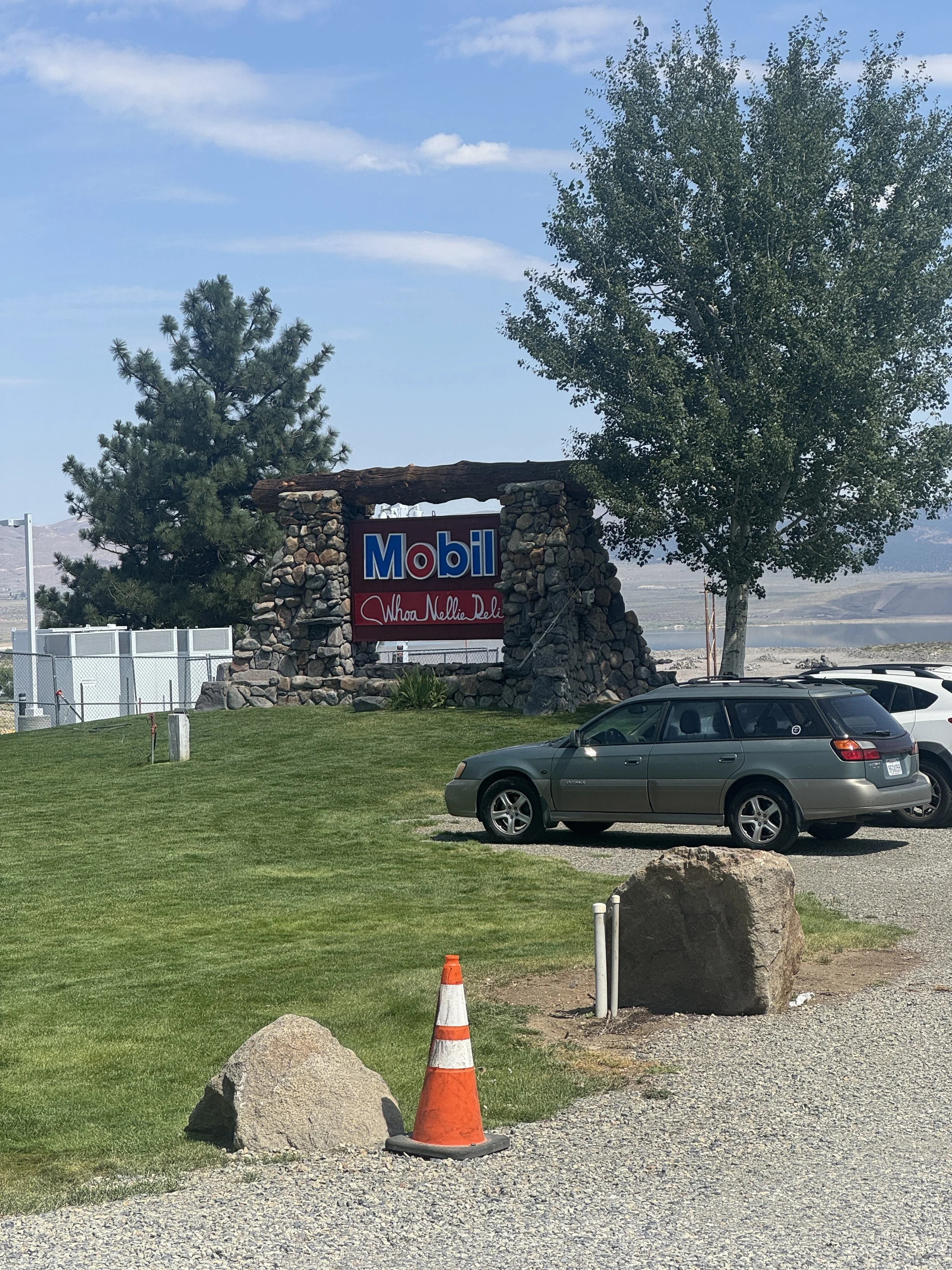 Mobil and Whoa Nellie Deli roadside sign framed by stone pillars with the Eastern Sierra landscape behind it in Lee Vining.