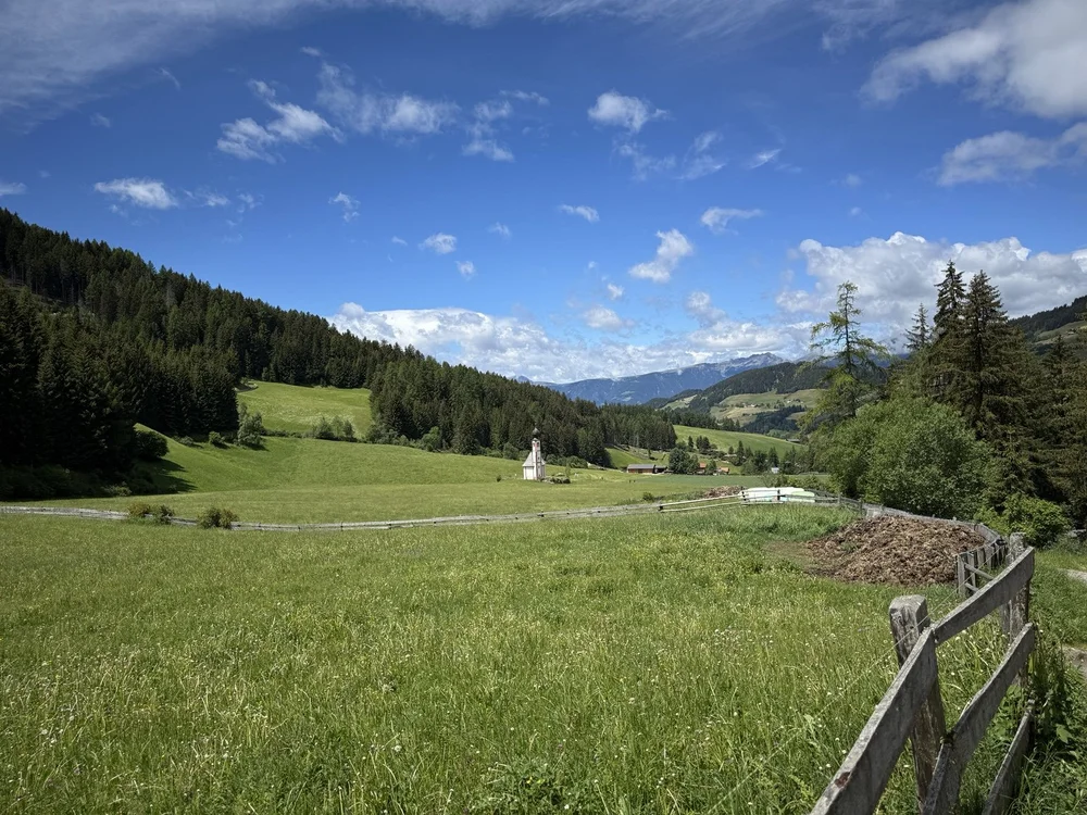 Santa Maddalena church surrounded by green Alpine meadows and forested hills in the Dolomites.
