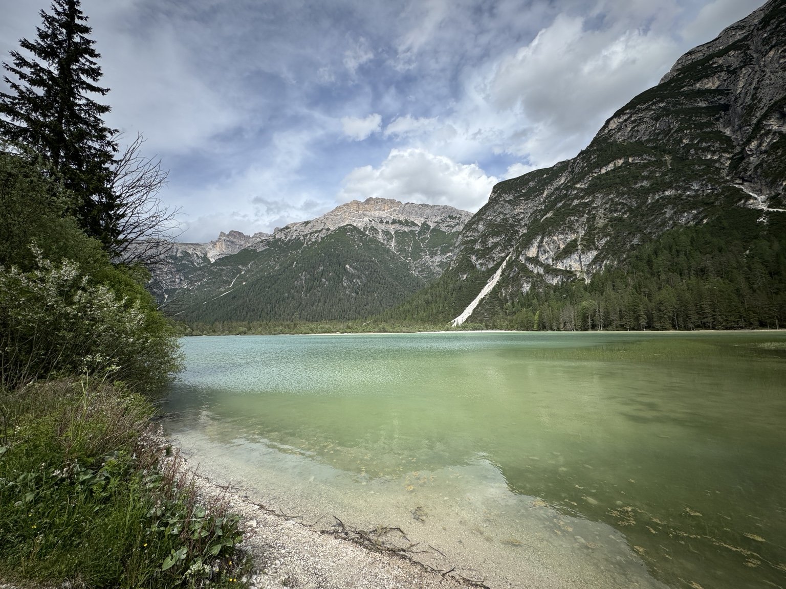 Panoramic view across the turquoise water of Lago di Landro framed by trees and Dolomite peaks.