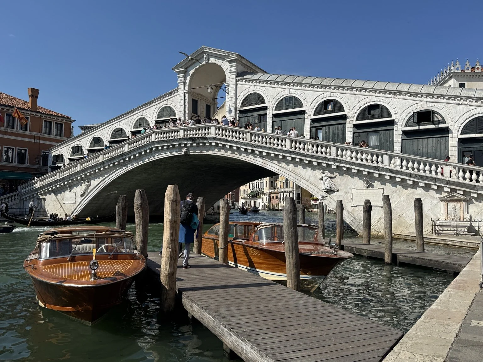 Rialto Bridge with polished wooden water taxis docked along the Grand Canal.
