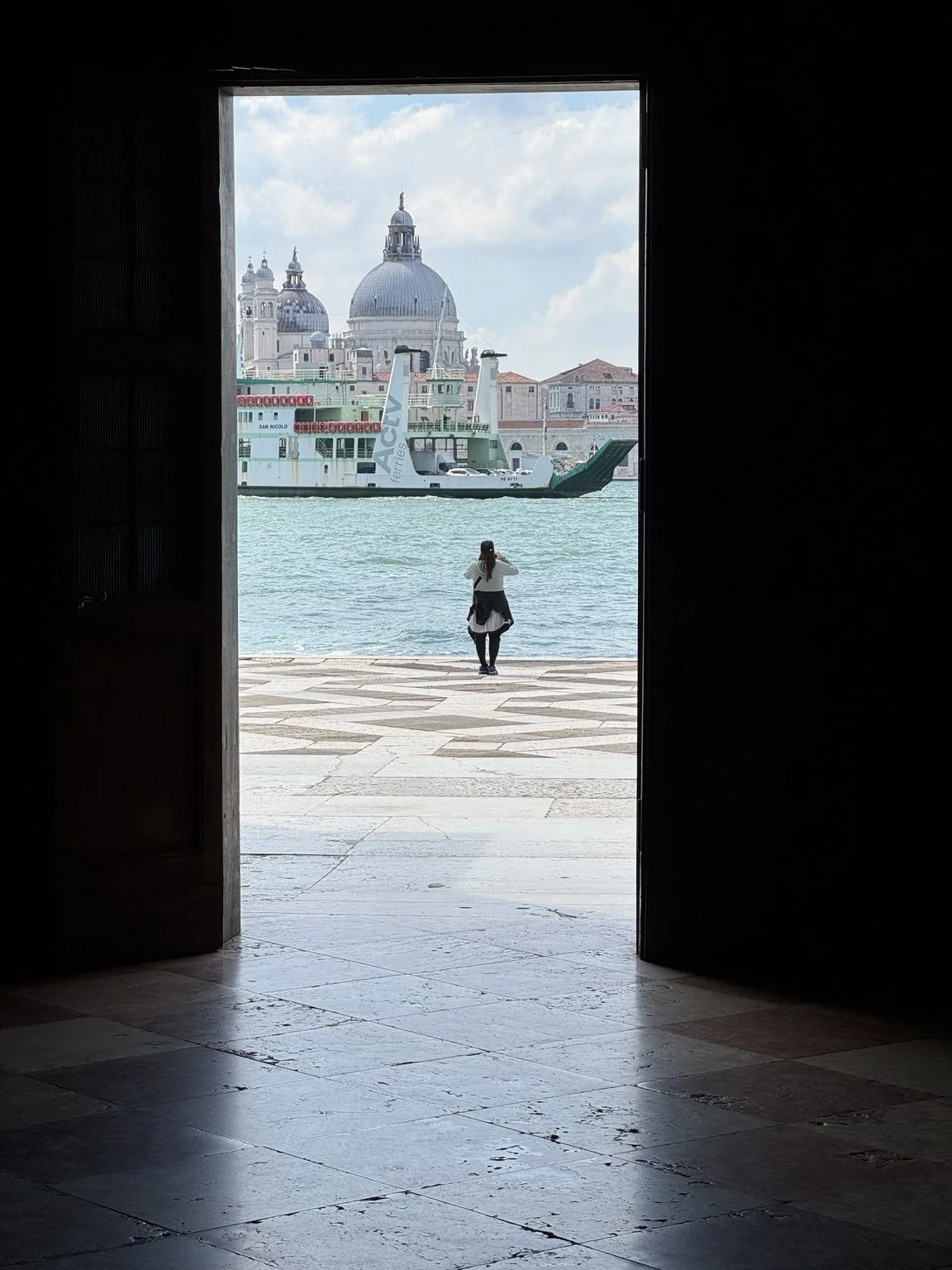 View through a dark doorway at San Giorgio Maggiore toward the Venetian lagoon, ferry and distant domes.