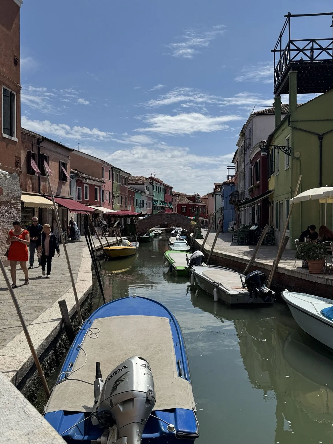 Colorful Burano canal with moored boats and an arched brick footbridge.