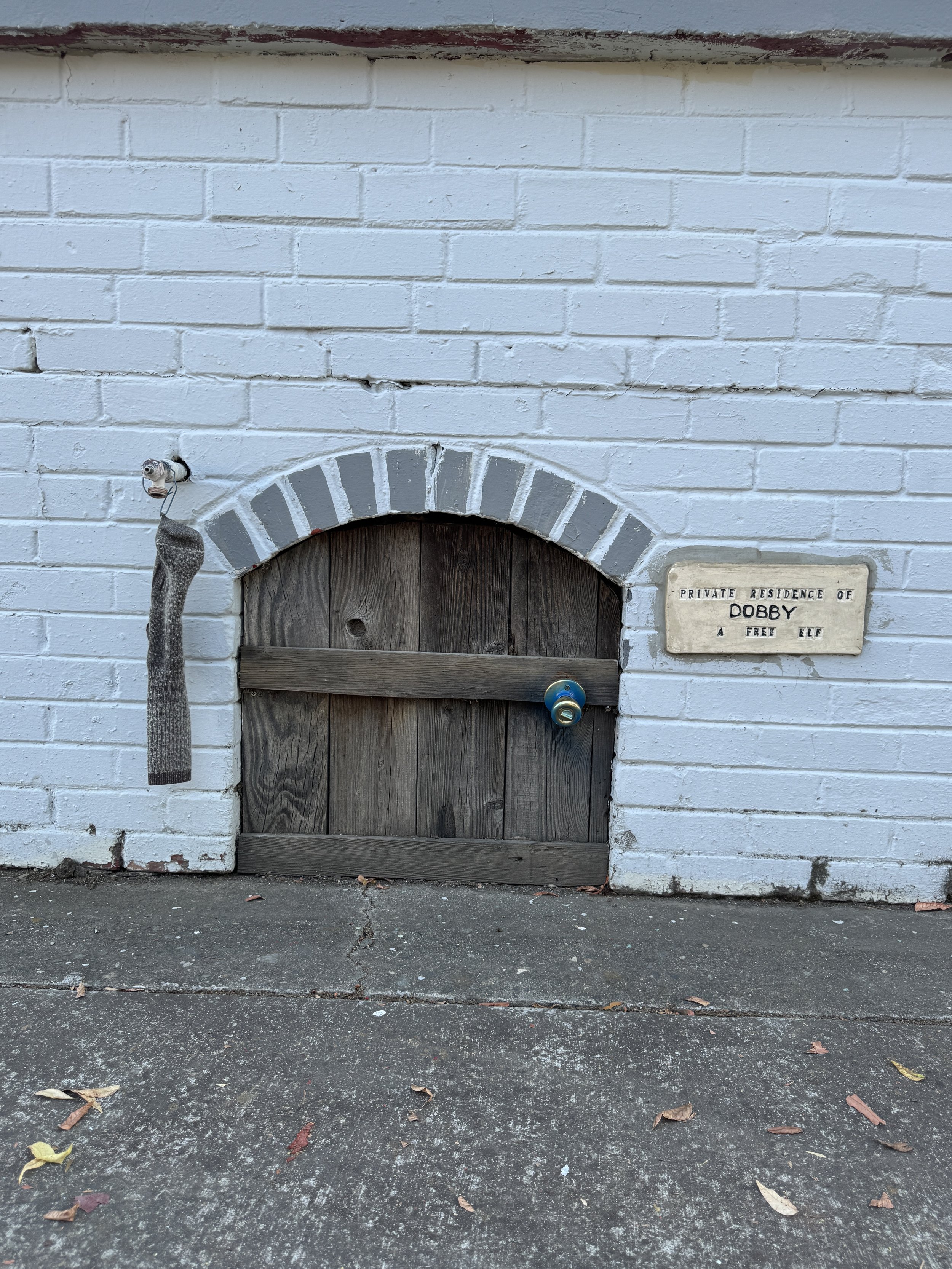 Miniature wooden door labeled Private Residence of Dobby, a Free Elf, set into a white brick wall.