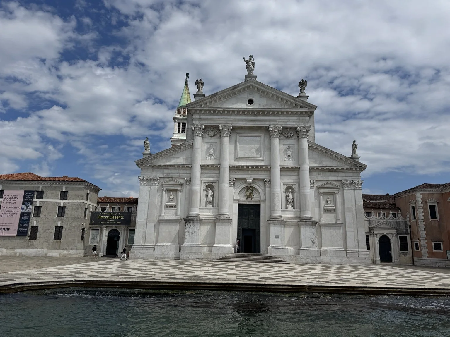 White marble façade of San Giorgio Maggiore viewed across the water beneath a cloudy blue sky.