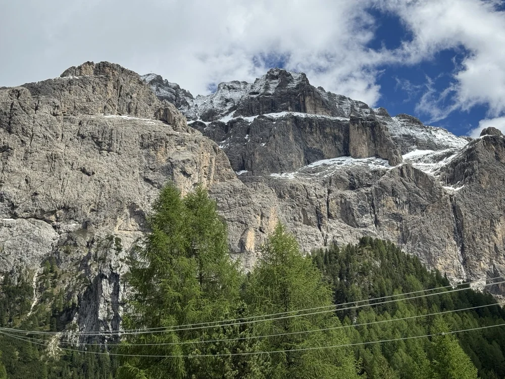 Close view of rugged, snow-dusted Dolomite cliffs above evergreen trees.