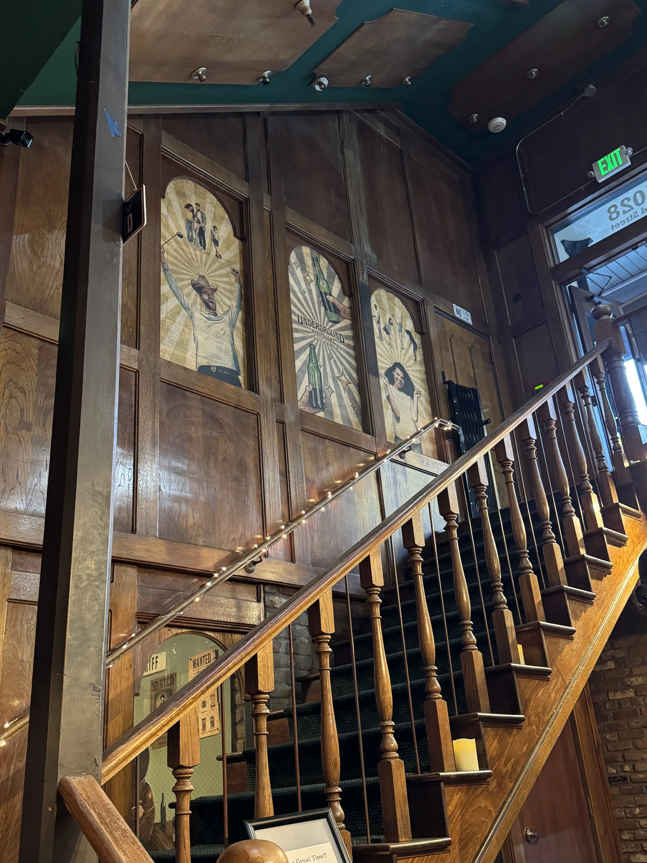 Wooden staircase leading down to Underground Mini Golf in Old Sacramento, decorated with vintage-style golf artwork and string lights.