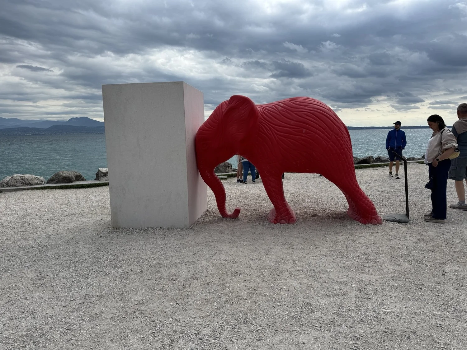 Red elephant sculpture beside Lake Garda under dramatic clouds in Sirmione