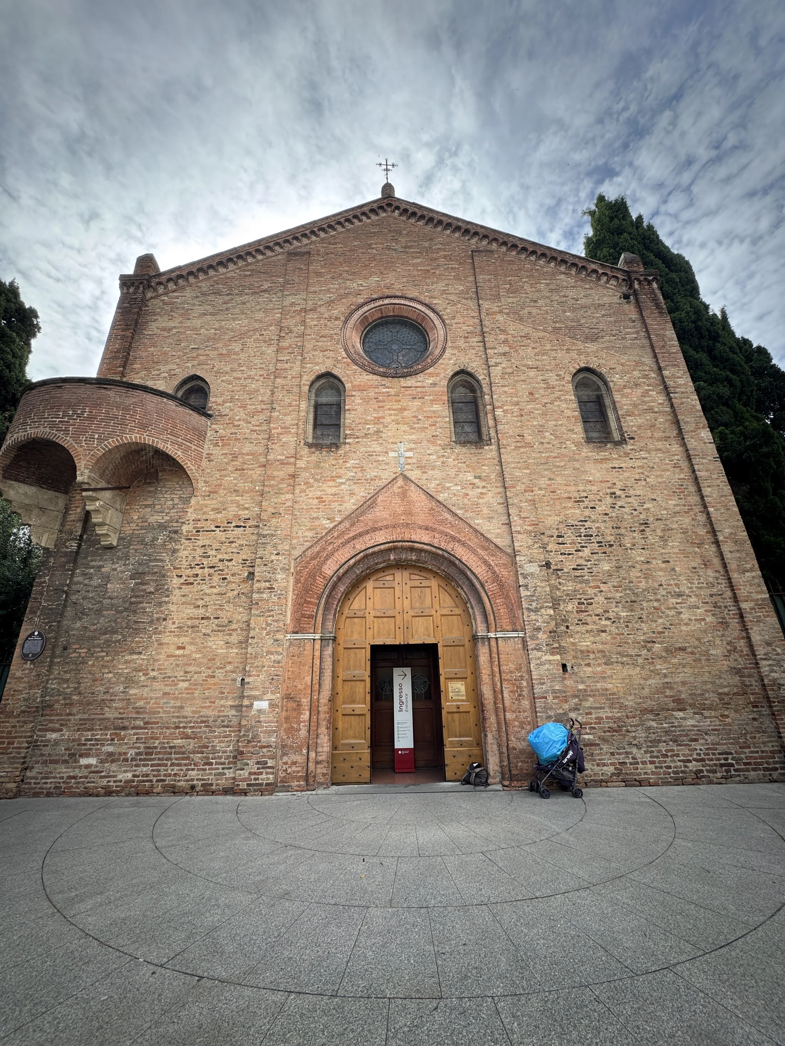 Brick facade and arched entrance of Bologna's Basilica di Santo Stefano beneath a dramatic sky.