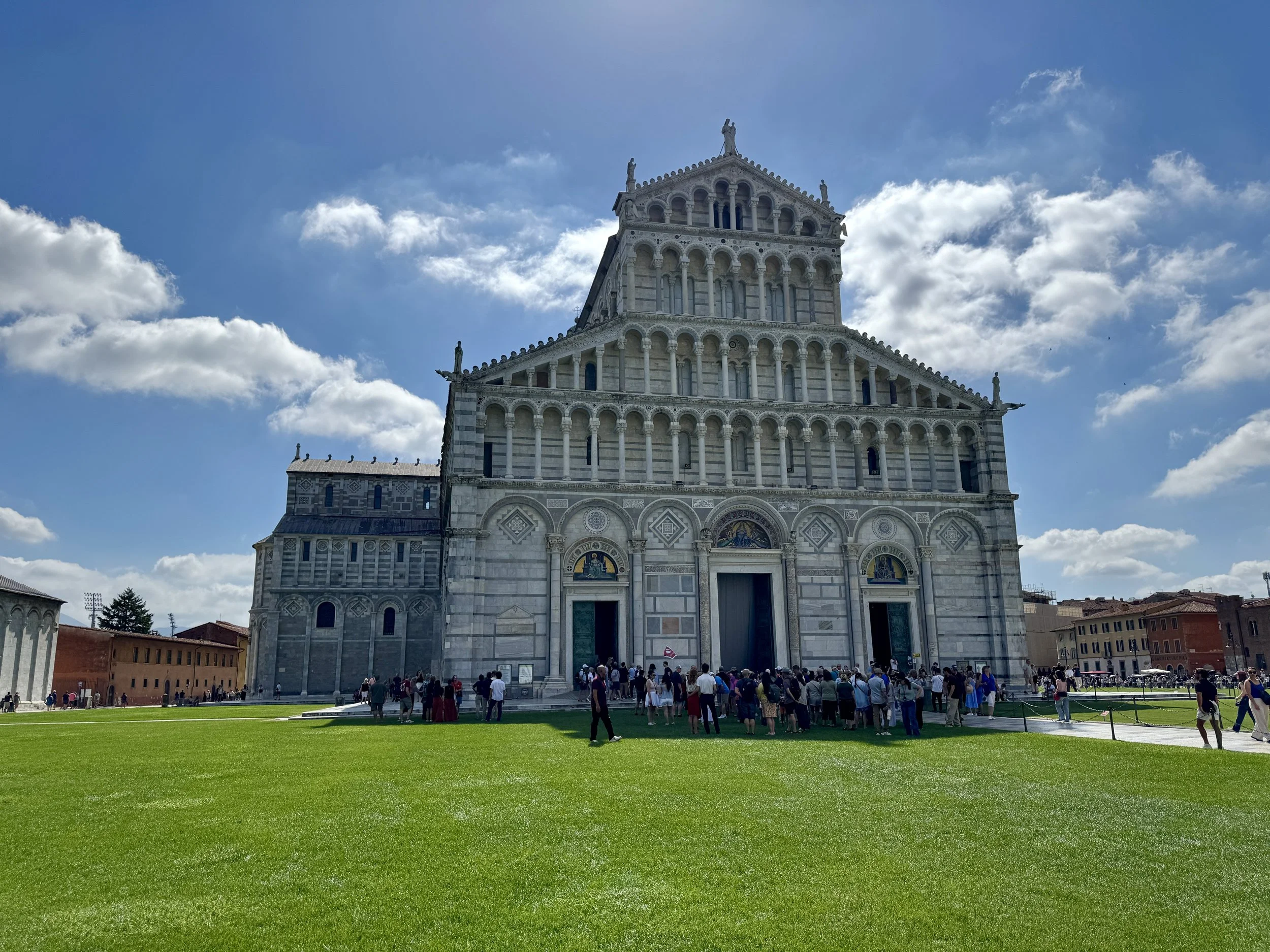 White marble façade of Pisa Cathedral beneath a dramatic blue sky.