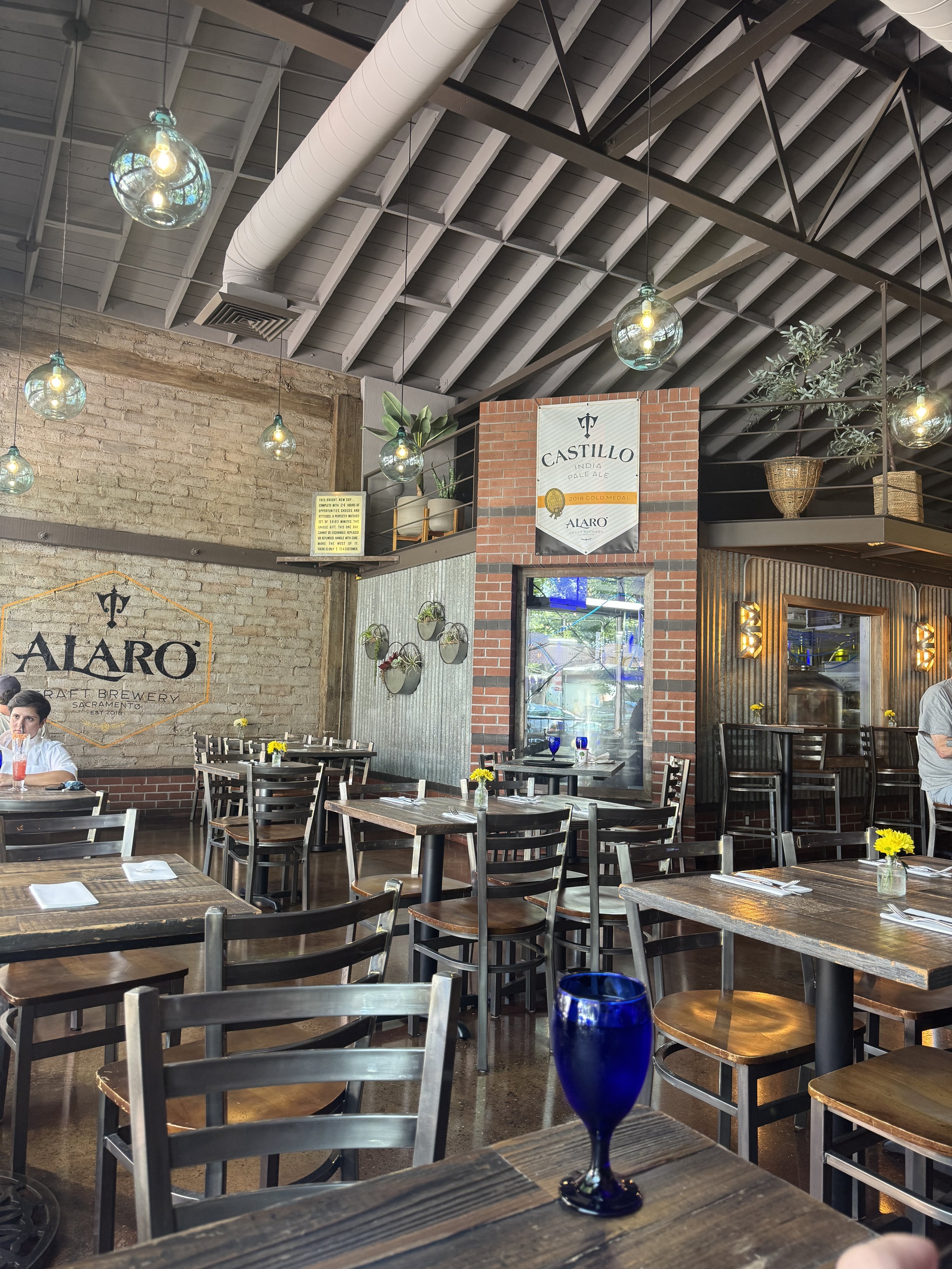 Warm brick-and-wood dining room with hanging globe lights inside Alaro Craft Brewery in Sacramento.