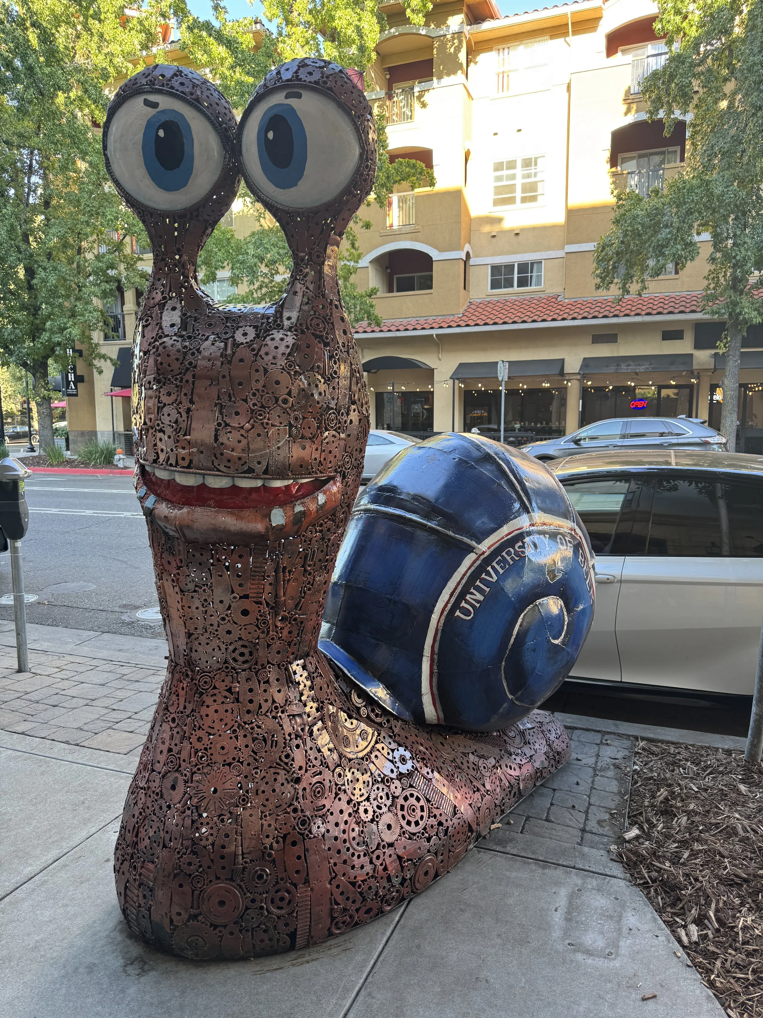 Oversized metal snail sculpture made from gears and other mechanical parts on a Sacramento sidewalk.