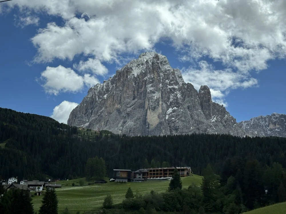 Snow-dusted Dolomite peak towering above forest and Alpine meadows.