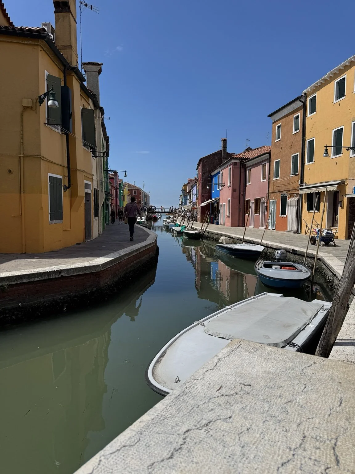 Sunny Burano canal lined with colorful houses and small boats.
