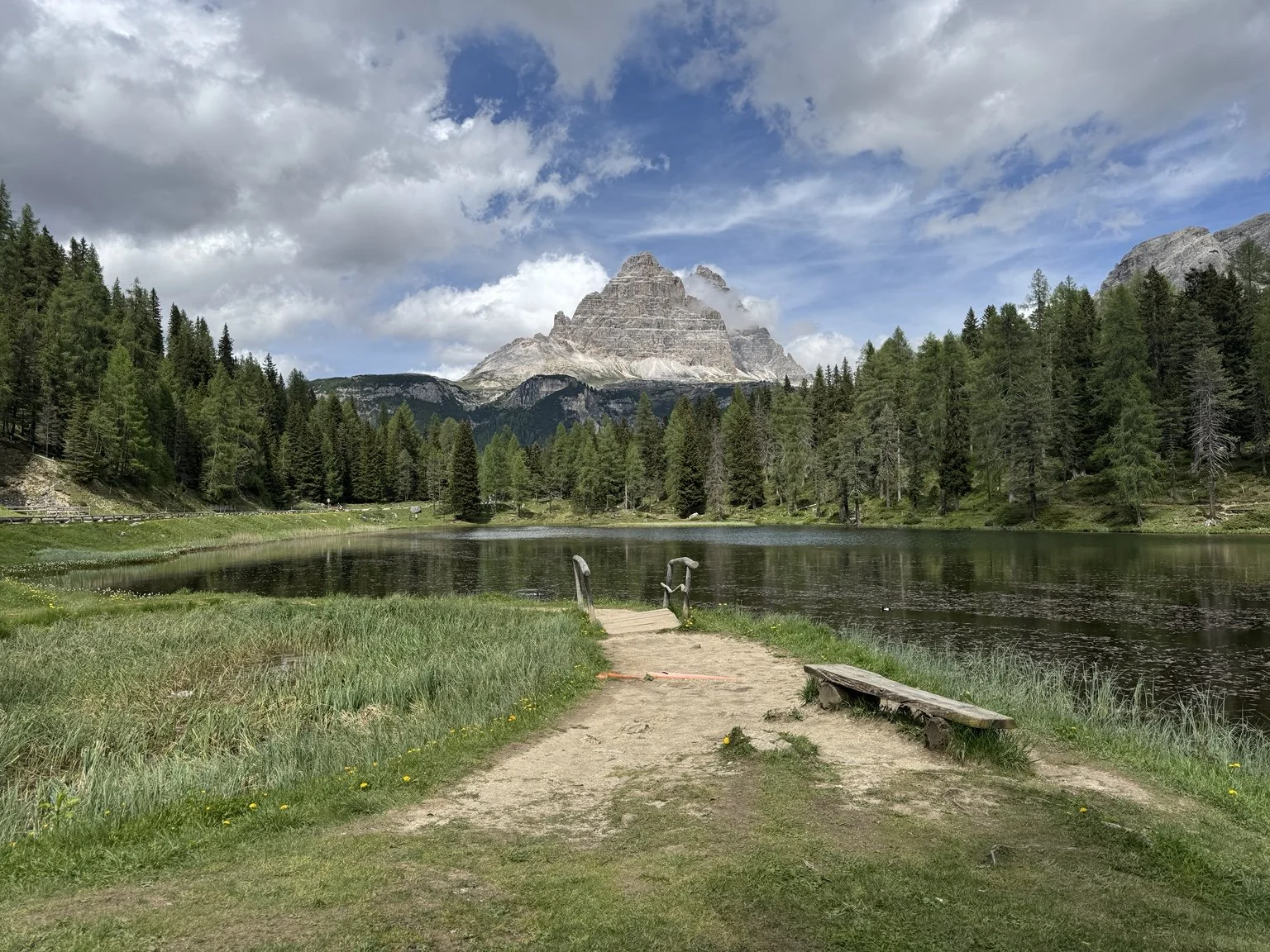 Lago d’Antorno with a lakeside path, wooden bench and rugged Dolomite mountains.