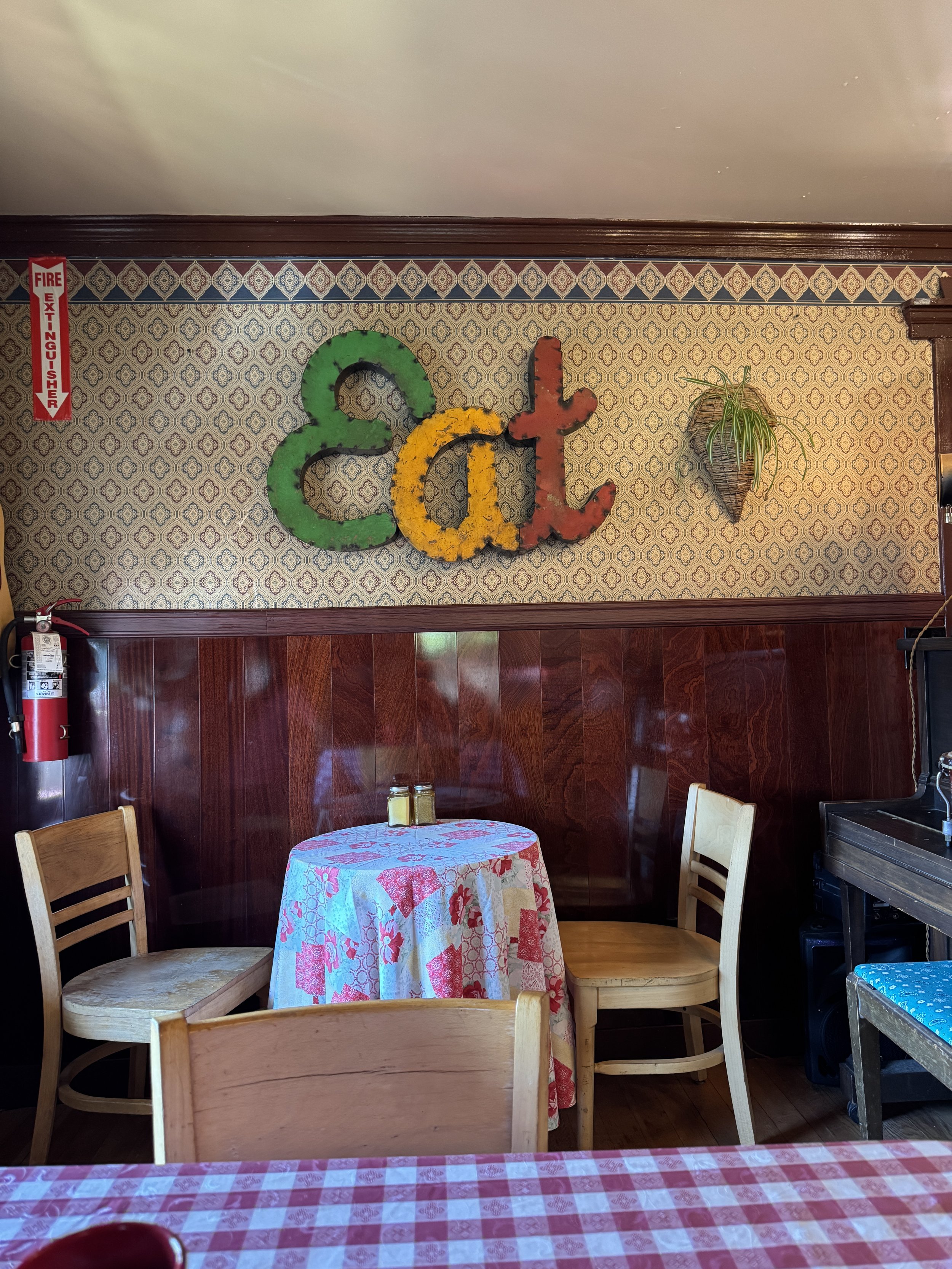 Quirky dining nook with vintage wallpaper and colorful eat sign inside the Cider House at Canvas Café in Virginia City.