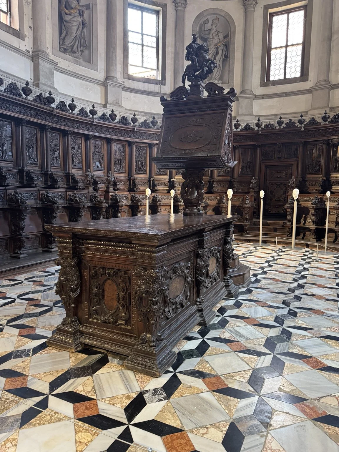 Ornate carved choir stalls and lectern inside San Giorgio Maggiore with small contemporary sculptures on display.