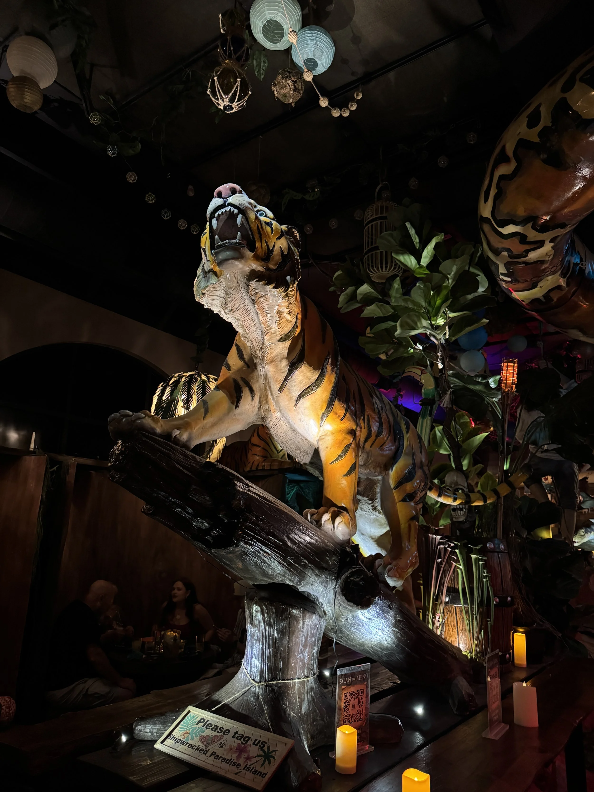Dramatically lit tiger animatronic perched on a tree branch inside Shipwrecked Paradise Island.