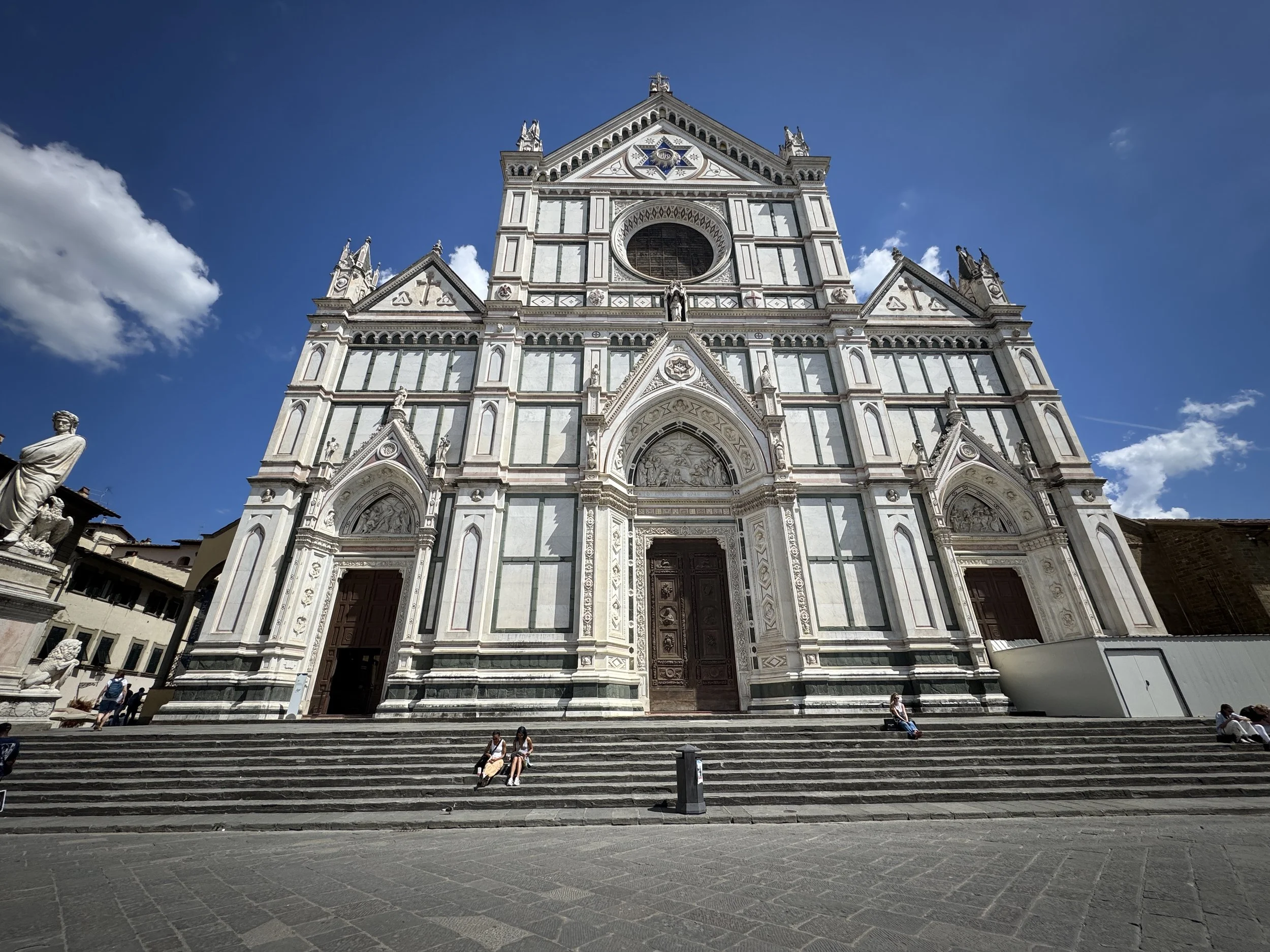 White, green and pink marble facade of Florence's Basilica di Santa Croce beneath a blue sky.